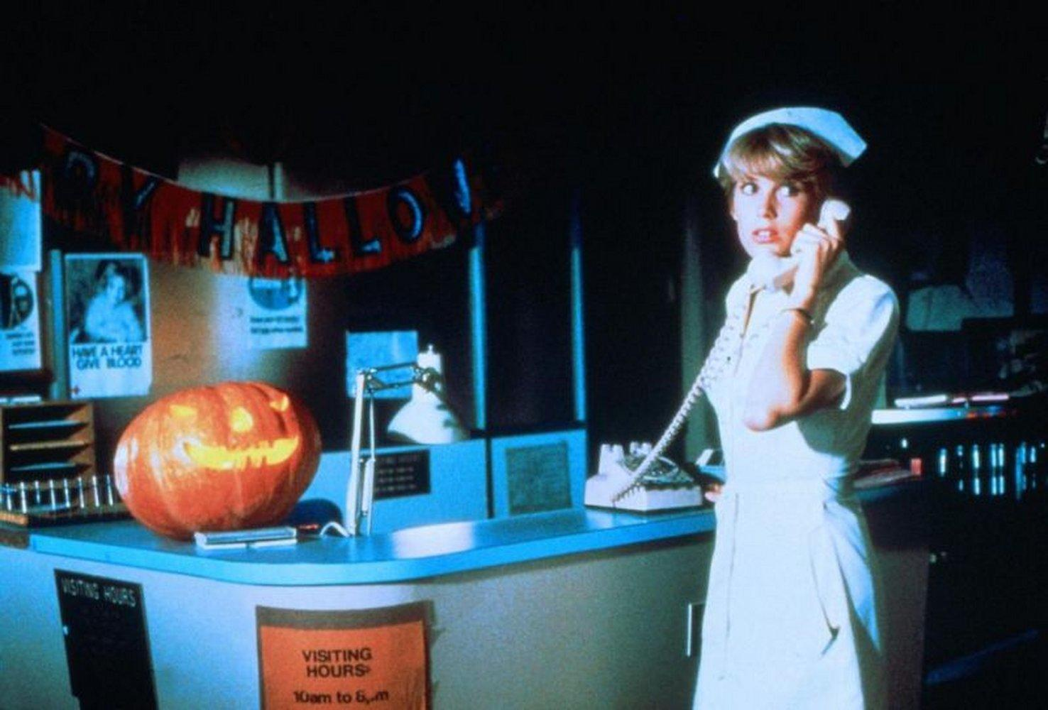 Eine Krankenschwester telefoniert in einem Krankenhaus. Ein geschnitzter Kürbis steht auf der Theke mit einem Banner mit der Aufschrift "Happy Halloween".