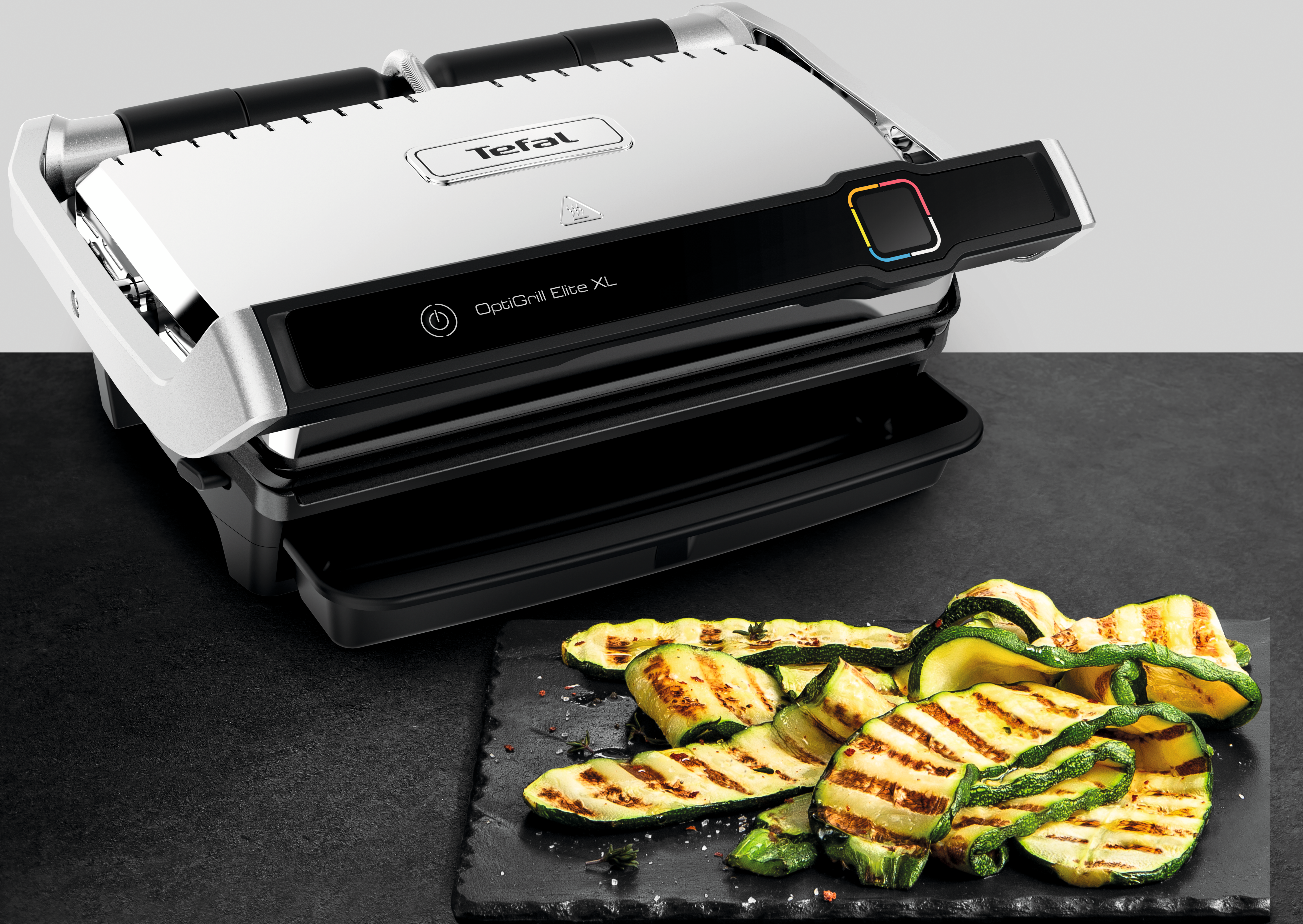 Ein OptiGrill Elite XL mit gegrillten Zucchini auf einem schwarzen Servierbrett. Der Grill ist silber und schwarz.