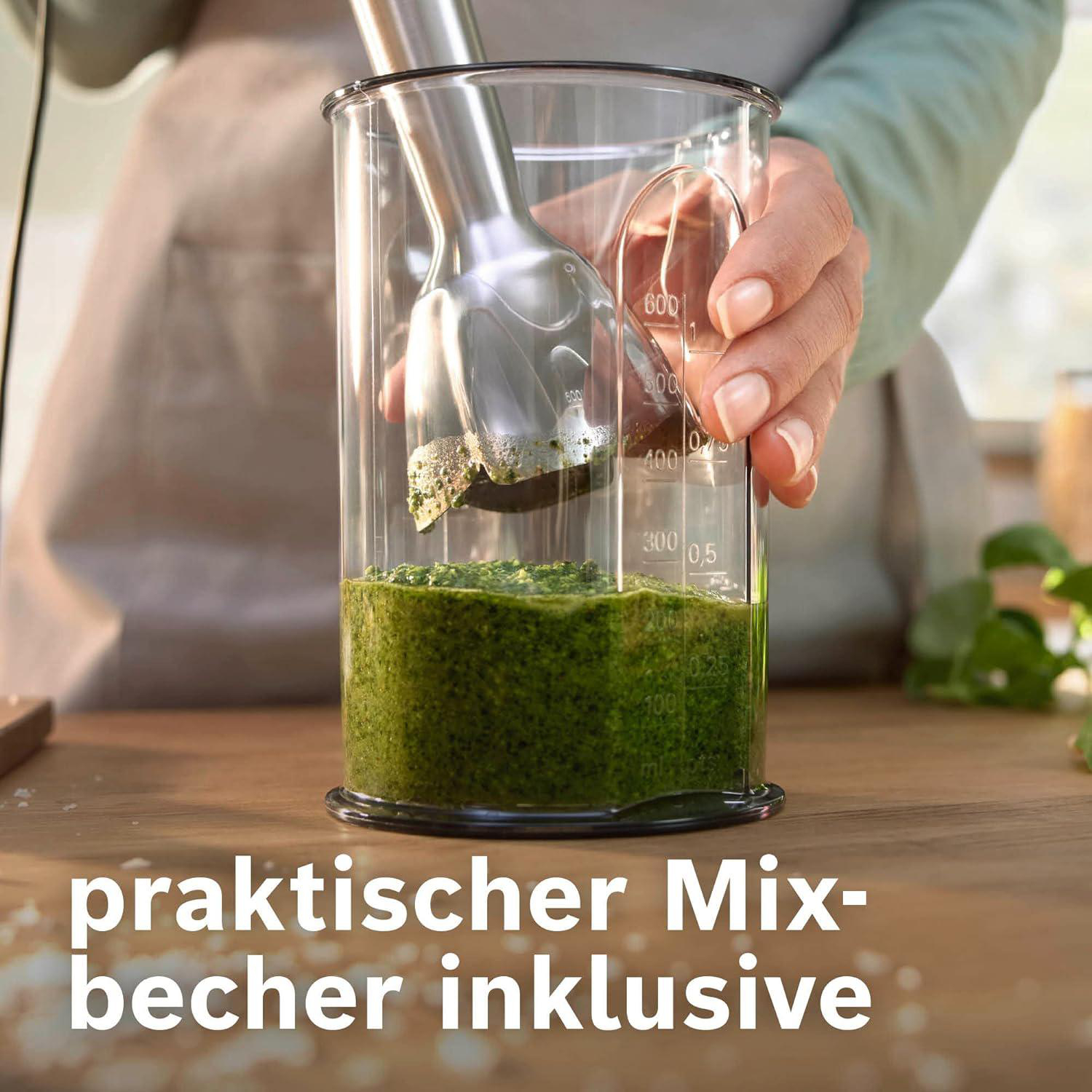 Eine Hand hält einen Mixer in einem Glas mit grünem Pesto. Der Text unten lautet 'praktischer Mixbecher inklusive'.