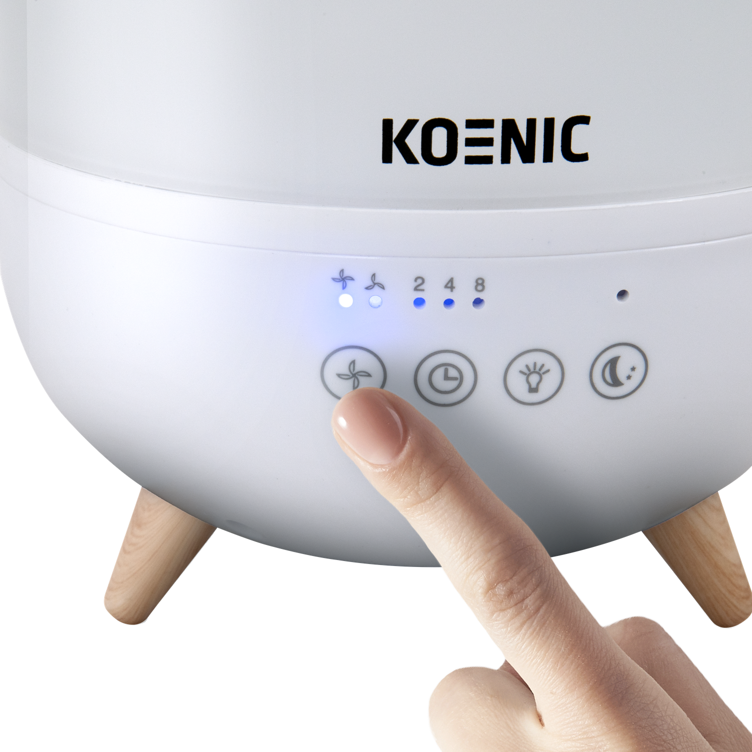 A white Koenic humidifier is shown. A finger presses the fan button. The humidifier has wooden legs and blue lights.