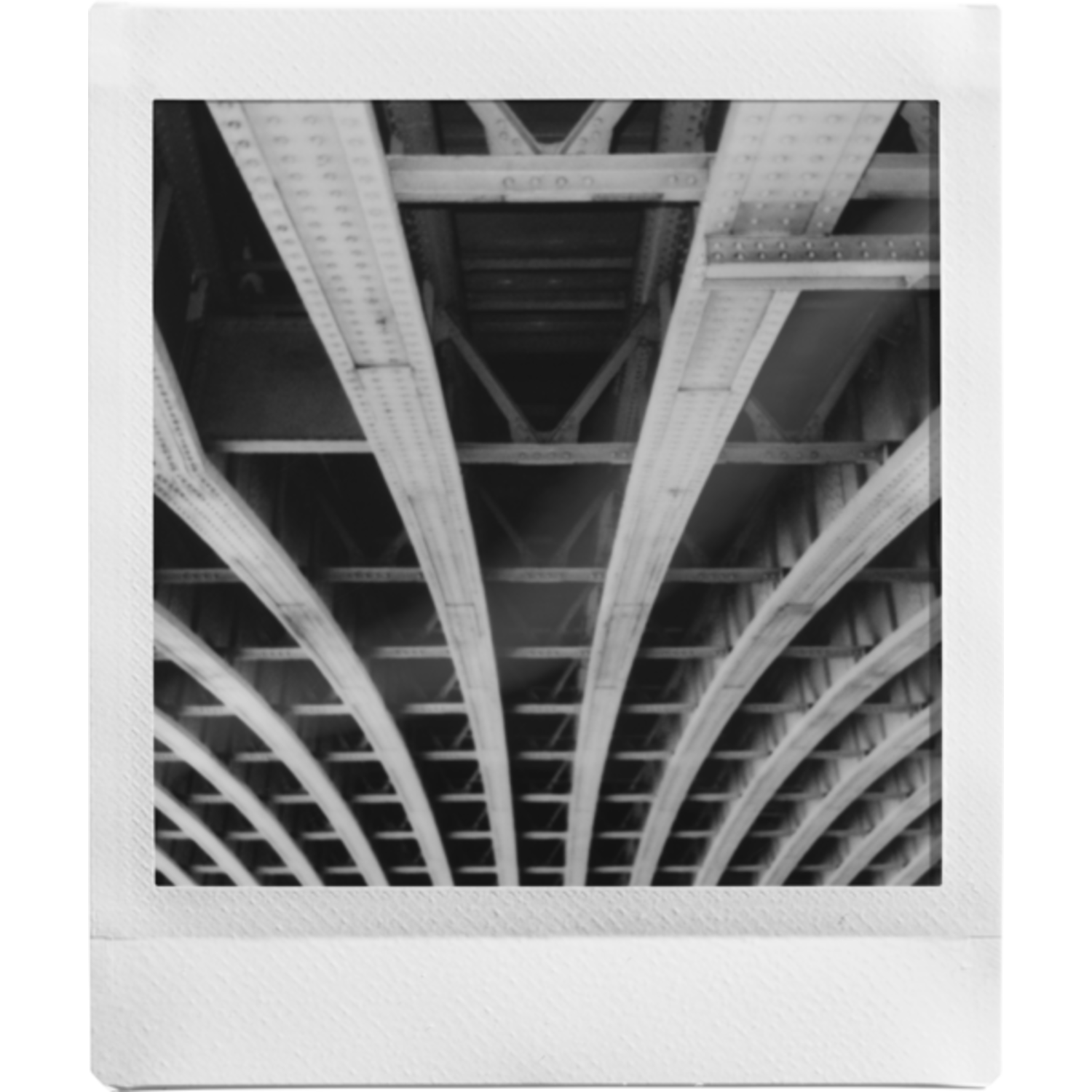 Zwart-wit afbeelding van de onderkant van een brug. Gebogen balken en metalen constructie zijn zichtbaar, waardoor een herhalend patroon met diepte ontstaat.