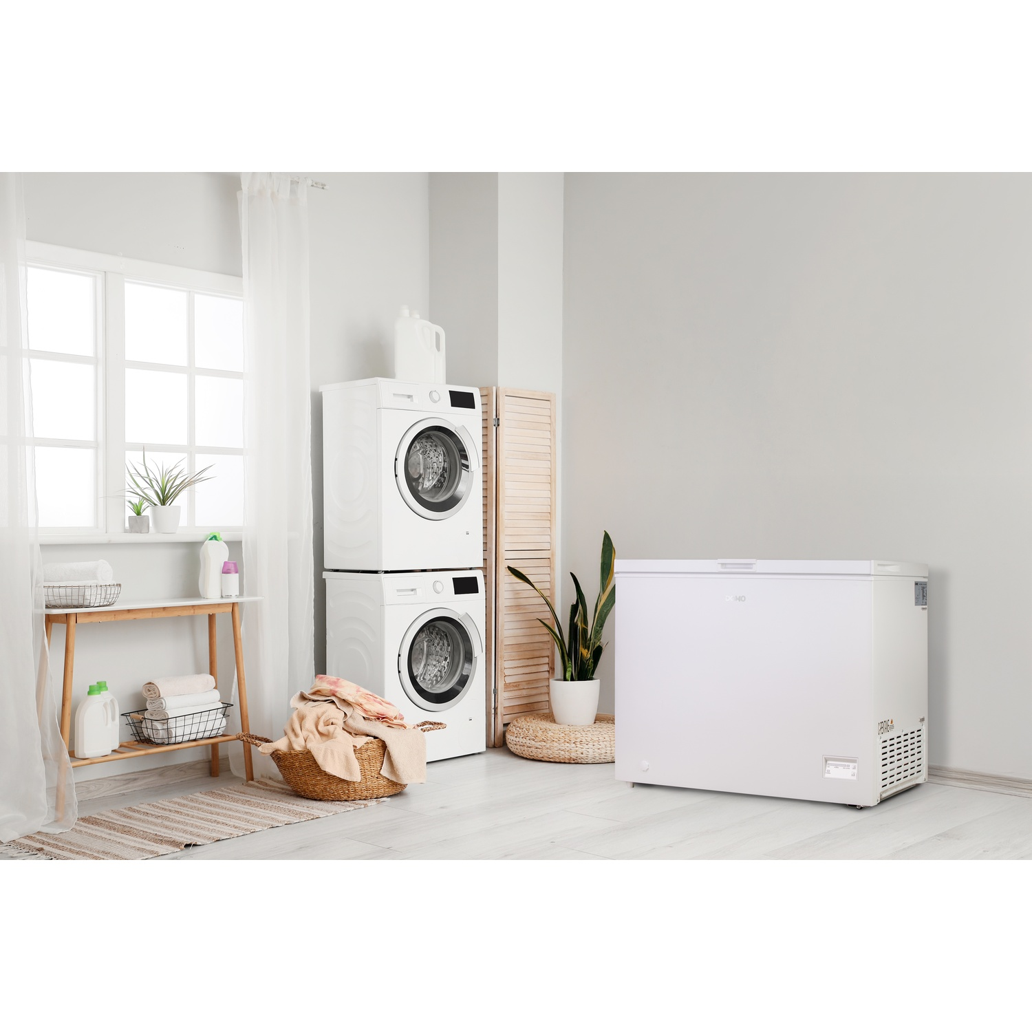 Buanderie avec lave-linge et sèche-linge empilés, congélateur coffre blanc et panier de linge. Plantes et fenêtre visibles.