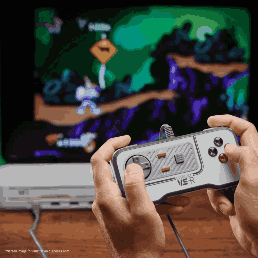 Manos sosteniendo un mando Evercade VS-R, jugando a un videojuego. La pantalla muestra una escena de juego pixelada. Consola en superficie de madera.