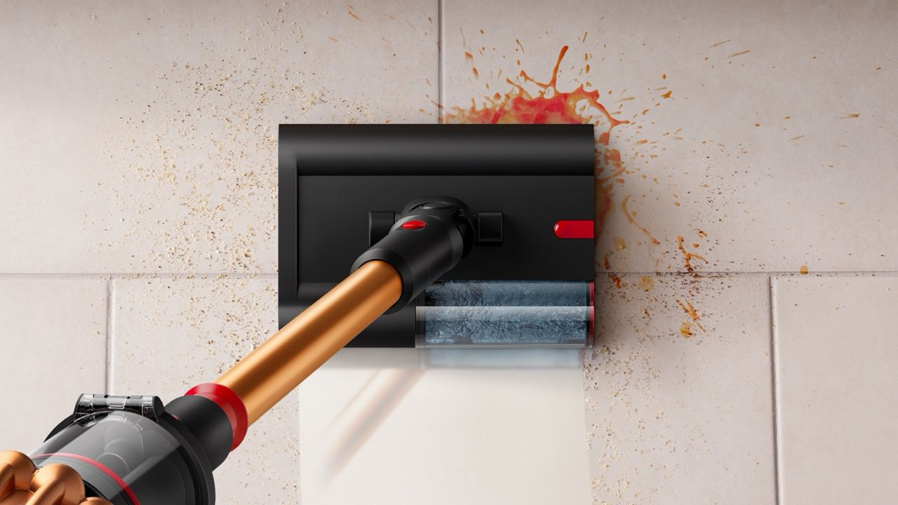 Głowica odkurzacza czyszcząca ścianę z plamami po jedzeniu. Odkurzacz jest czarny i złoty. Widoczne są rozpryski jedzenia.