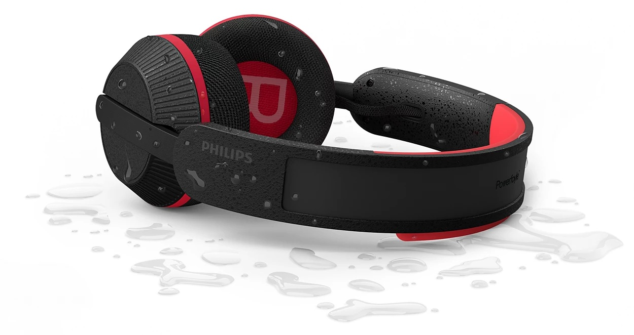 Czarne i czerwone słuchawki Philips Powerfy na białej powierzchni z kroplami wody. Słuchawki są mokre.