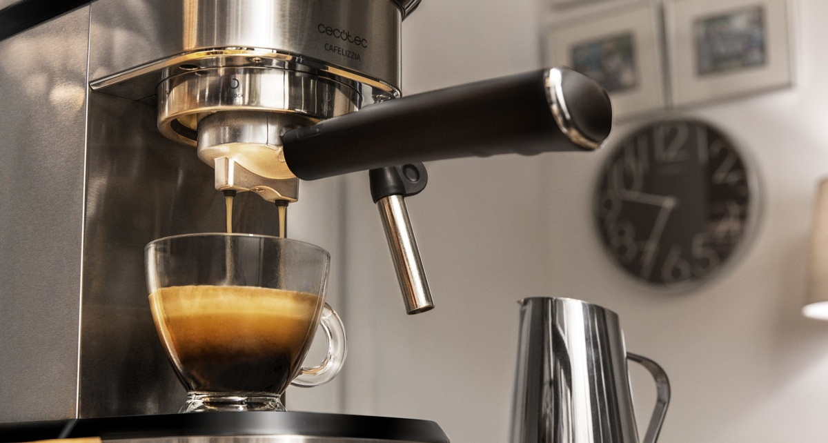 Ekspres do kawy dozuje kawę do szklanki. Widoczna maszyna ze stali nierdzewnej, czarny uchwyt i dzbanek na mleko.