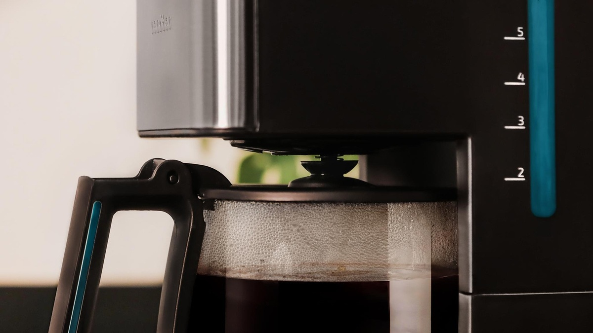 Zbliżenie ekspresu do kawy parzącego kawę. Karafka jest wypełniona ciemnym płynem. Maszyna jest czarna i srebrna.
