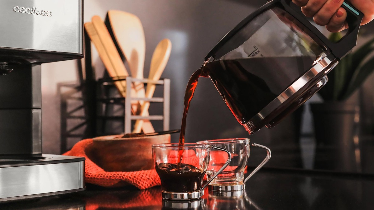 Kawa wlewana do dwóch szklanych filiżanek. Po lewej stronie ekspres do kawy. Drewniane łyżki i miska w tle.