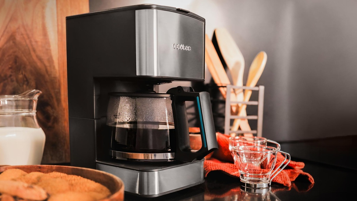 Czarny ekspres do kawy ze szklaną karafką stoi na blacie. Obok znajdują się dwie szklanki i dzbanek mleka. Drewniane łyżki w tle.