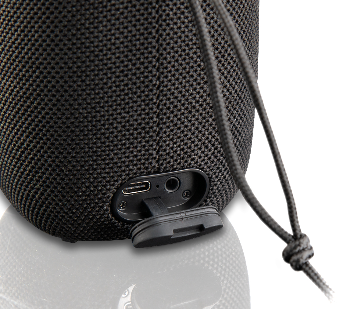 Czarny głośnik z portem USB i klapką ochronną. Czarny sznurek zwisa z góry. Tło jest białe.