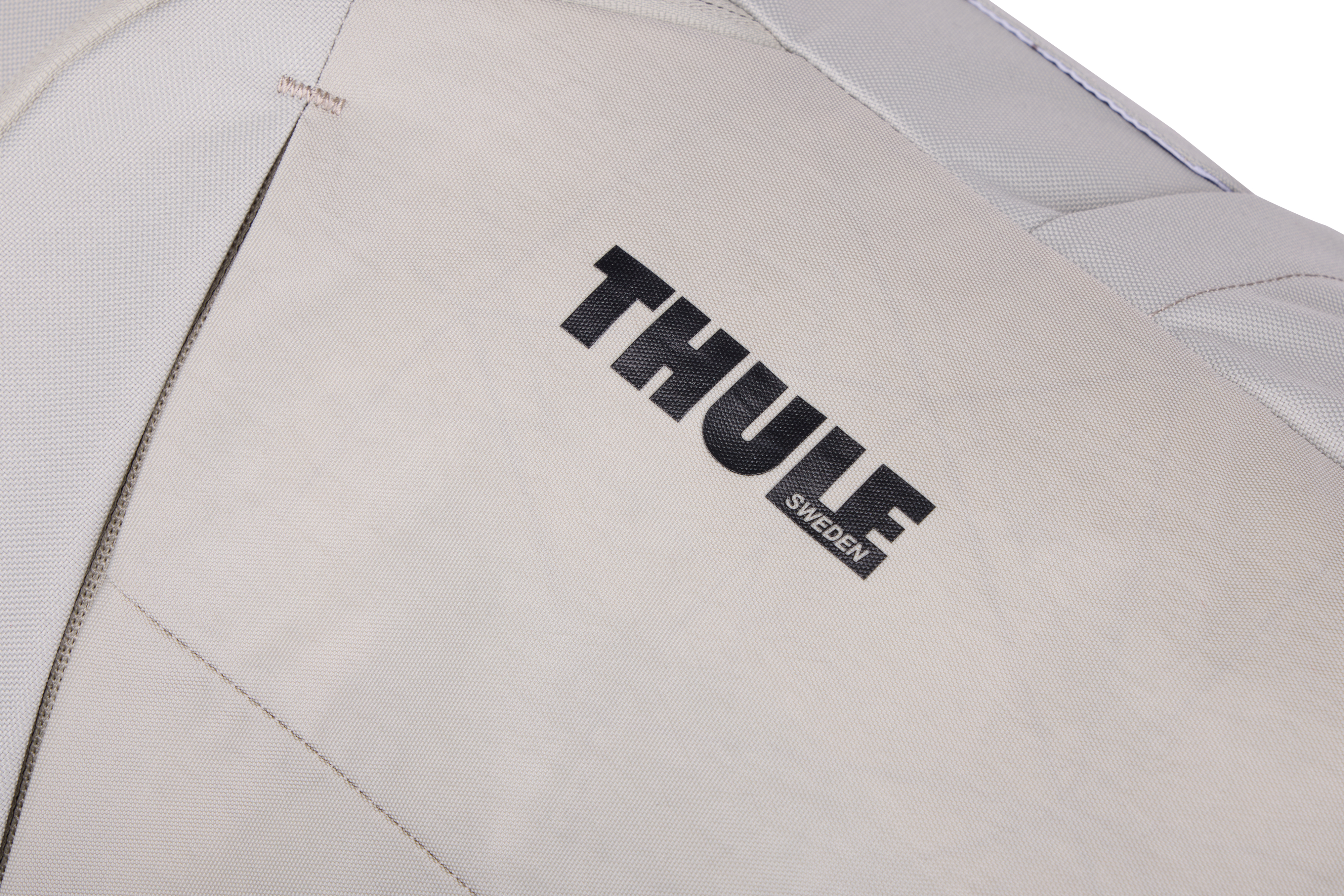 Thule çantasının yakın çekimi. Logo, açık gri bir yüzey üzerinde siyahtır. Dikişler ve dikiş yerleri görünür.