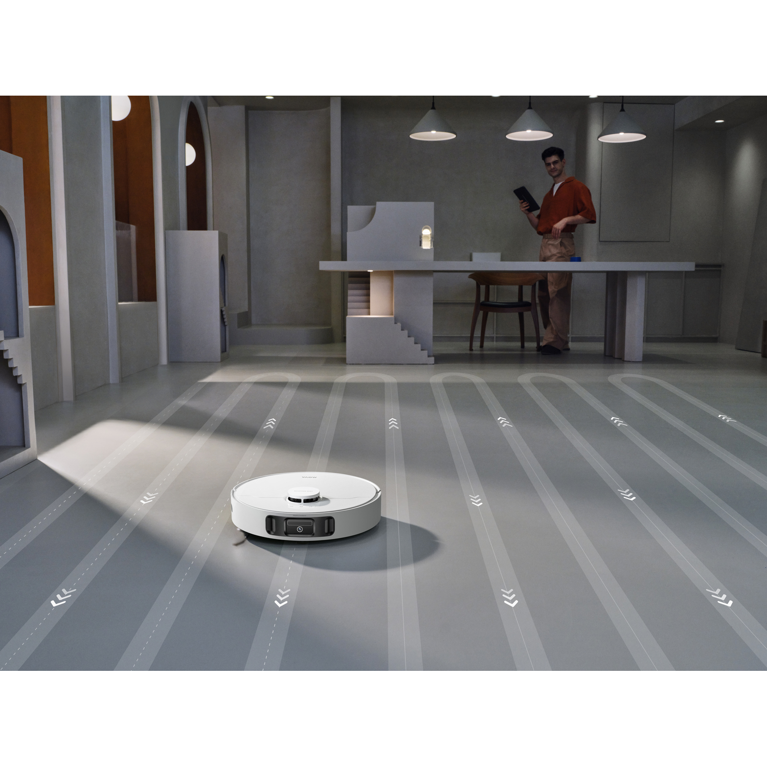 A white robotic vacuum cleaner on a grey floor with a man in the background holding a tablet.