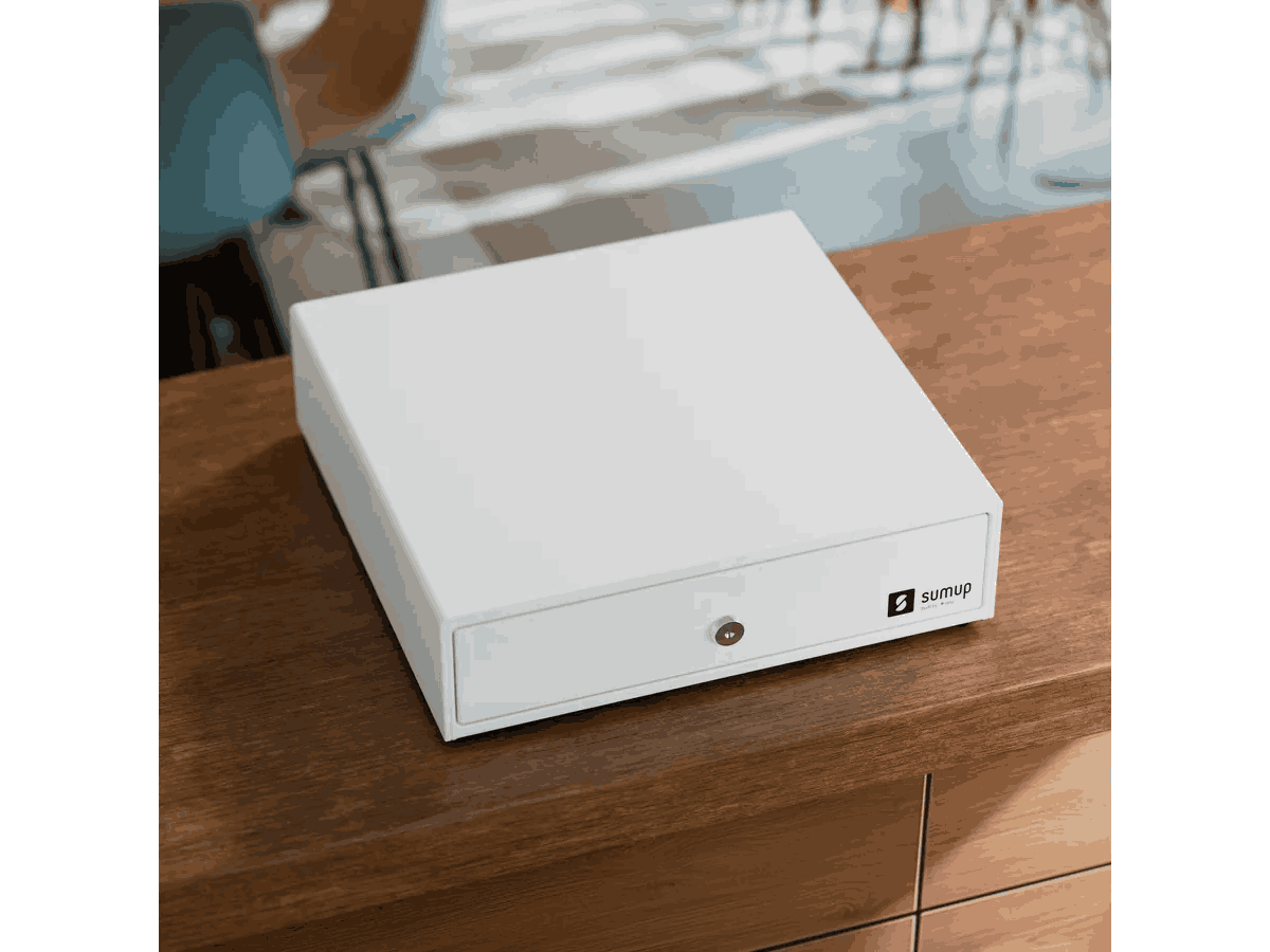 Una caja registradora blanca SumUp está sobre una superficie de madera. La caja está cerrada, con cerradura y logo visibles.