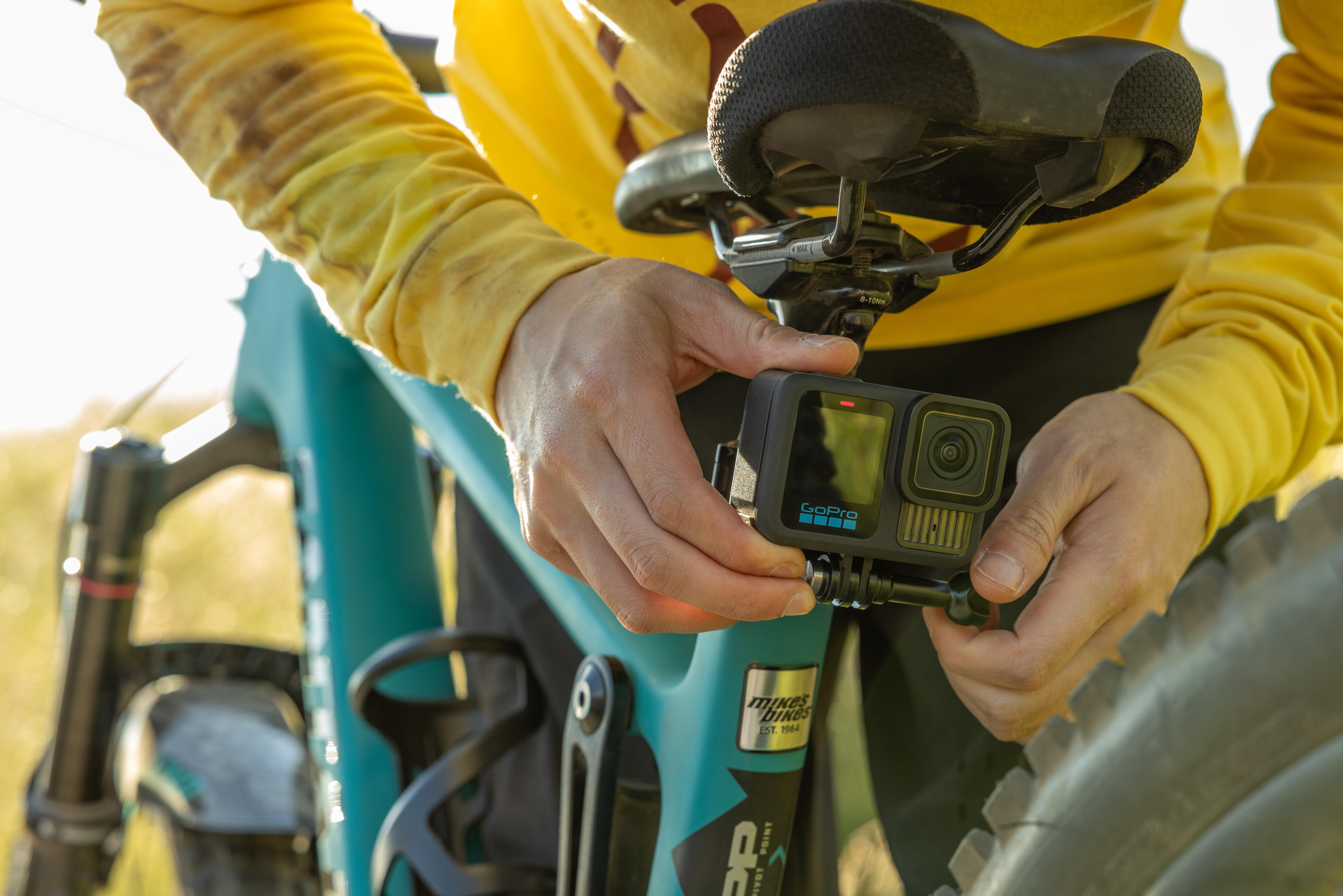 Eine Person befestigt eine GoPro-Kamera an einem Fahrrad. Die Person trägt ein gelbes Langarmhemd. Das Fahrrad ist blaugrün.