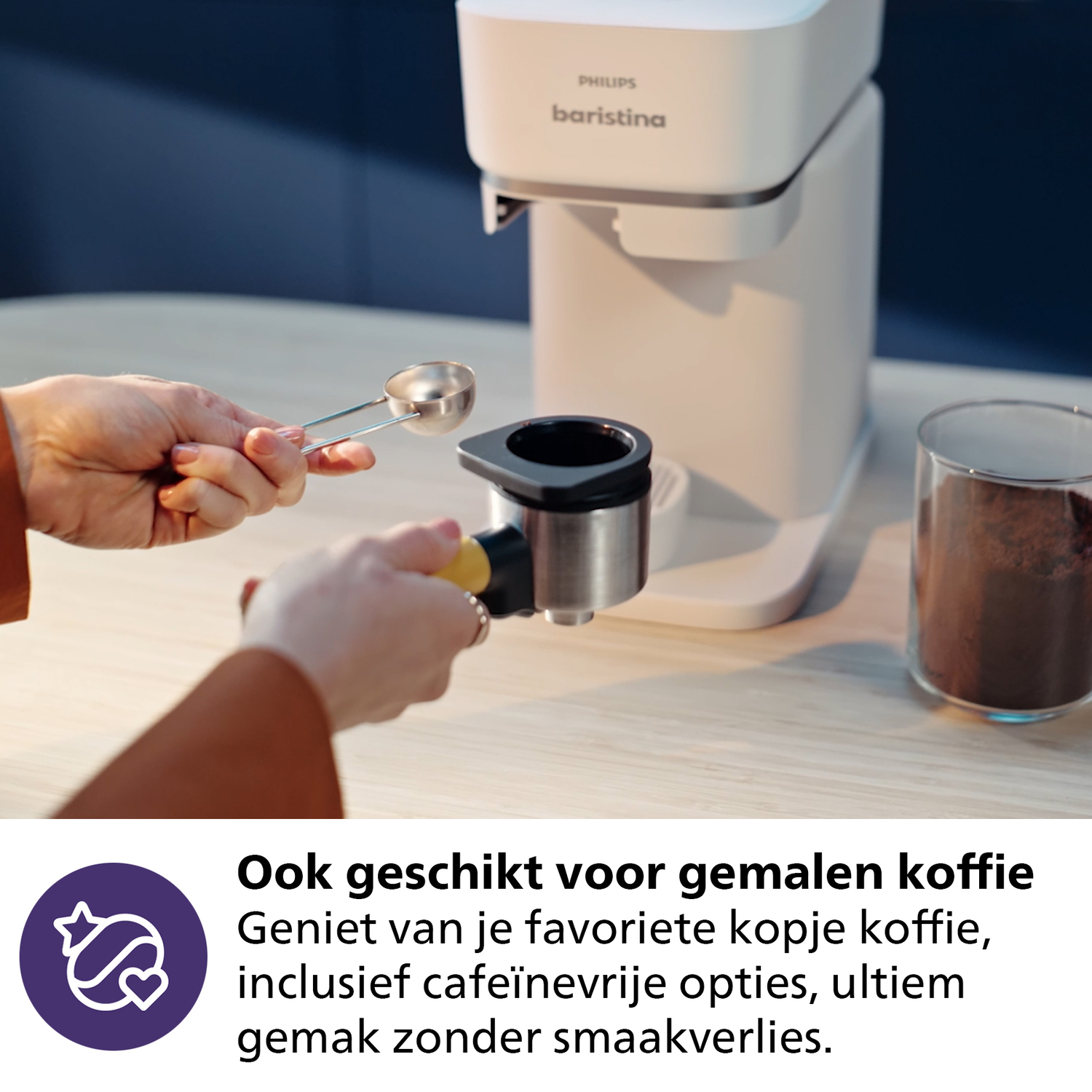 Een persoon houdt een koffielepel en een filterdrager vast. Een witte koffiemachine staat op een lichte houten tafel naast een potje gemalen koffie.