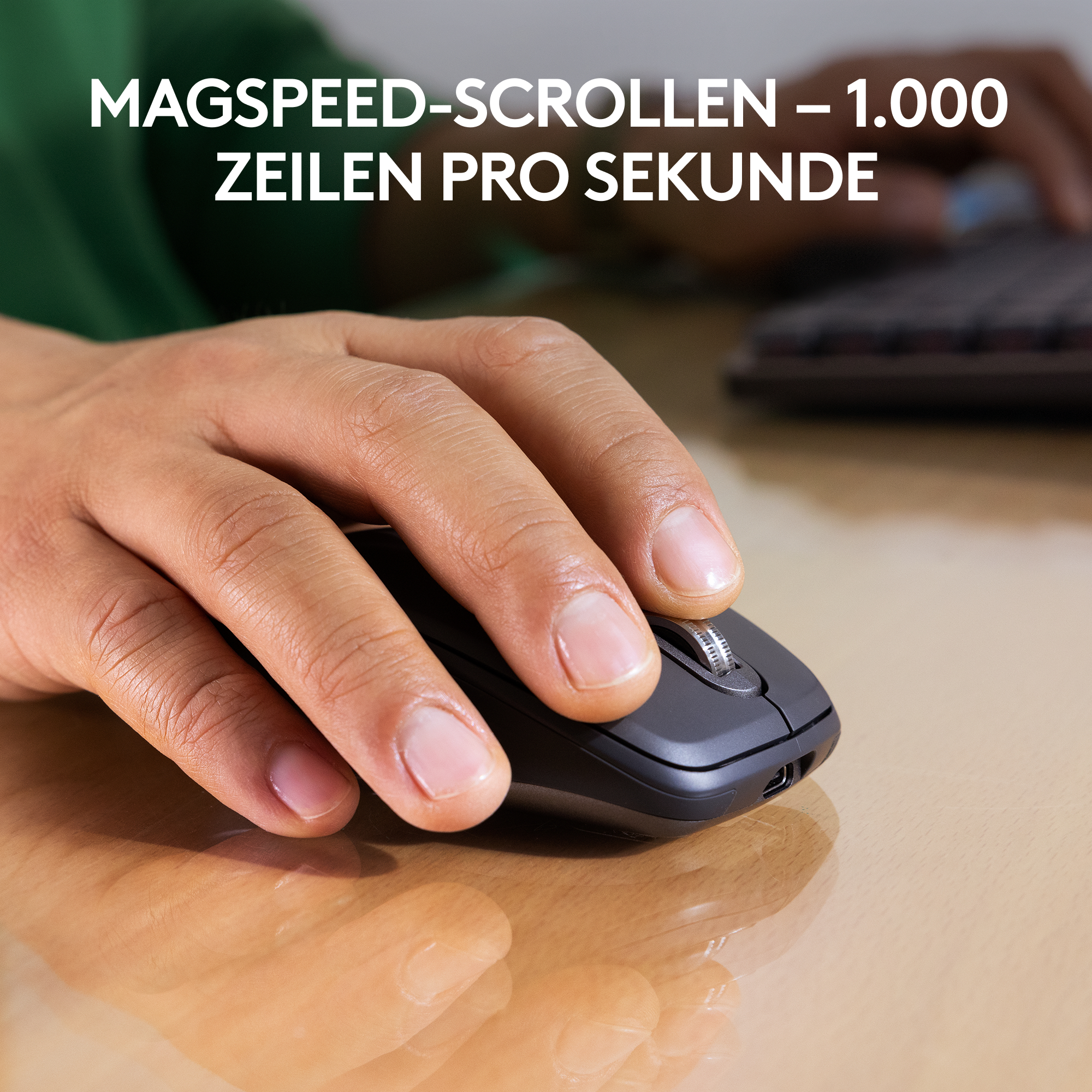 Eine Hand benutzt eine schwarze Computermaus auf einer hellbraunen Oberfläche. Die Maus befindet sich in der Nähe einer Tastatur. Text: MagSpeed-Scrollen.