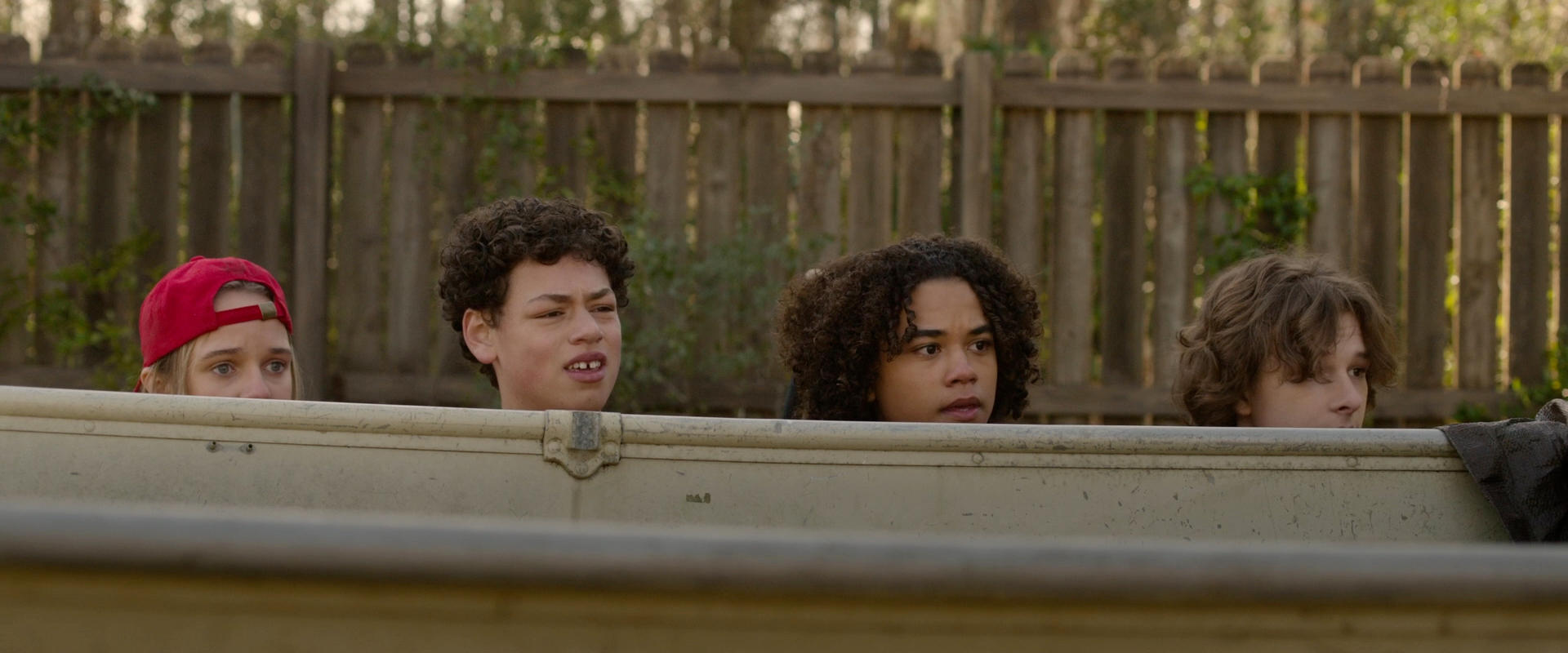 Vier junge Leute blicken über den Rand eines Bootes. Im Hintergrund ist ein Holzzaun zu sehen.