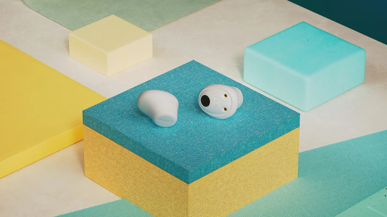 Białe słuchawki leżą na niebieskim pudełku. Inne kolorowe bloki i kształty w tle. Scena jest dobrze oświetlona.