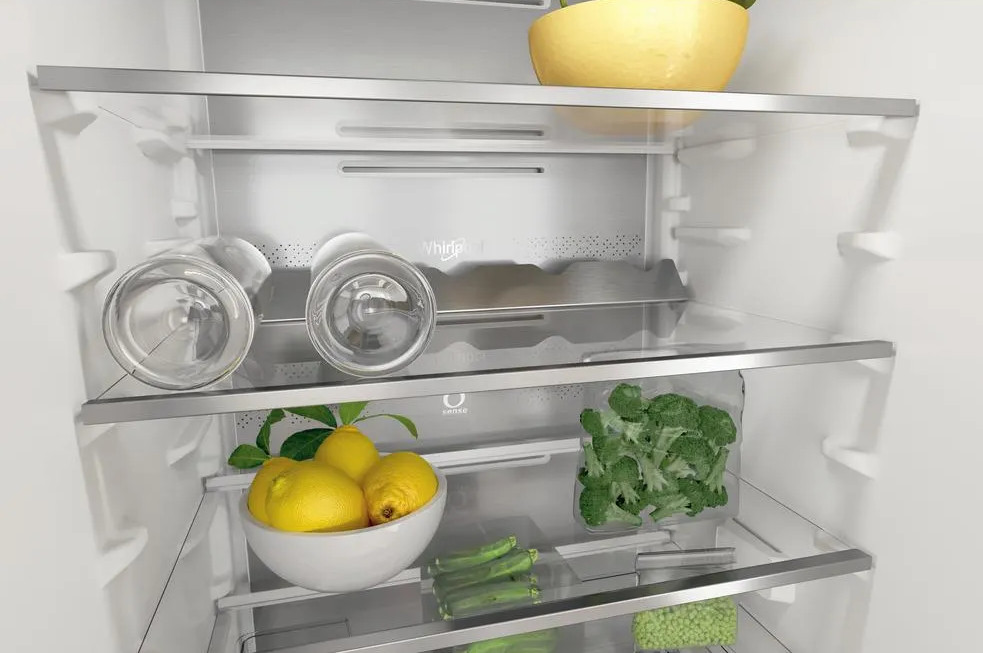 Wnętrze lodówki ze szklanymi półkami. Zawiera miskę cytryn, brokuły, groszek, szkło i żółtą miskę.