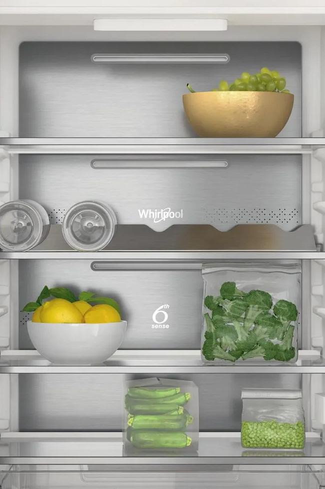 Wewnątrz lodówki: winogrona, cytryny, brokuły, groszek i cukinia są przechowywane. Lodówka ma logo Whirlpool i 6th Sense.
