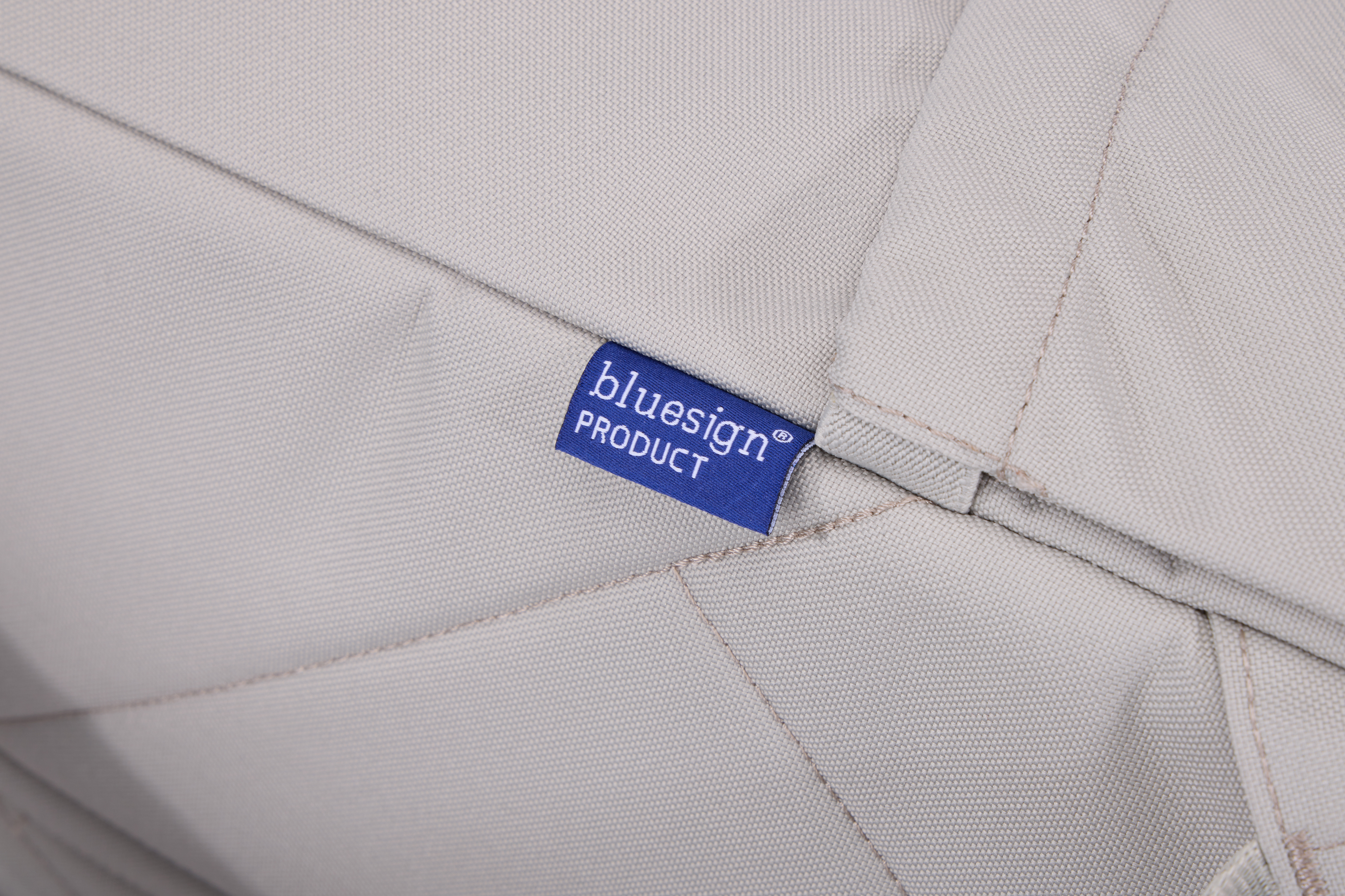 Açık gri kumaşın yakın çekimi, üzerinde 'bluesign PRODUCT' yazan mavi bir etiketle.