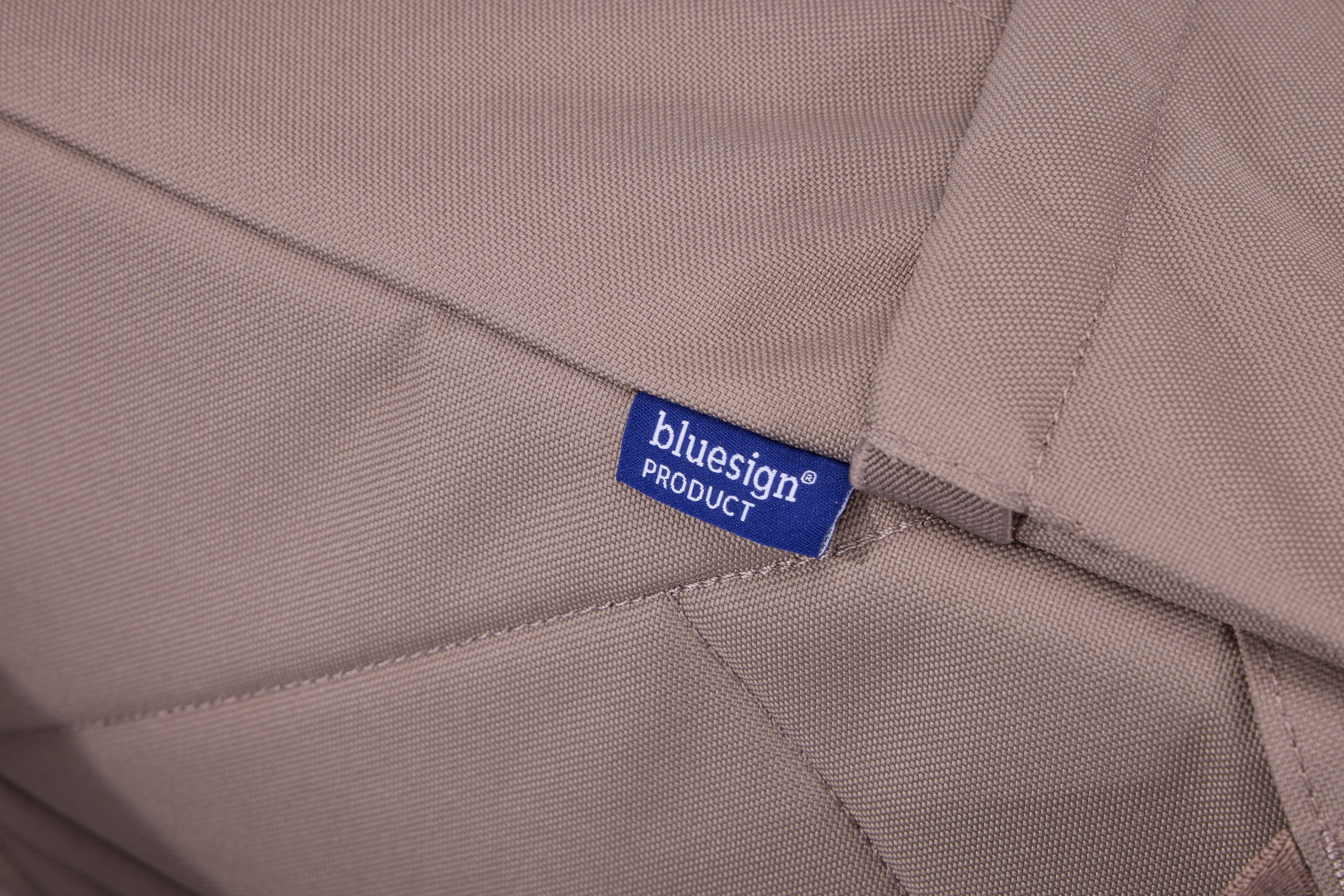 "bluesign® PRODUCT" yazan mavi bir etiket bulunan, bej renkli bir kumaşın yakın çekimi.