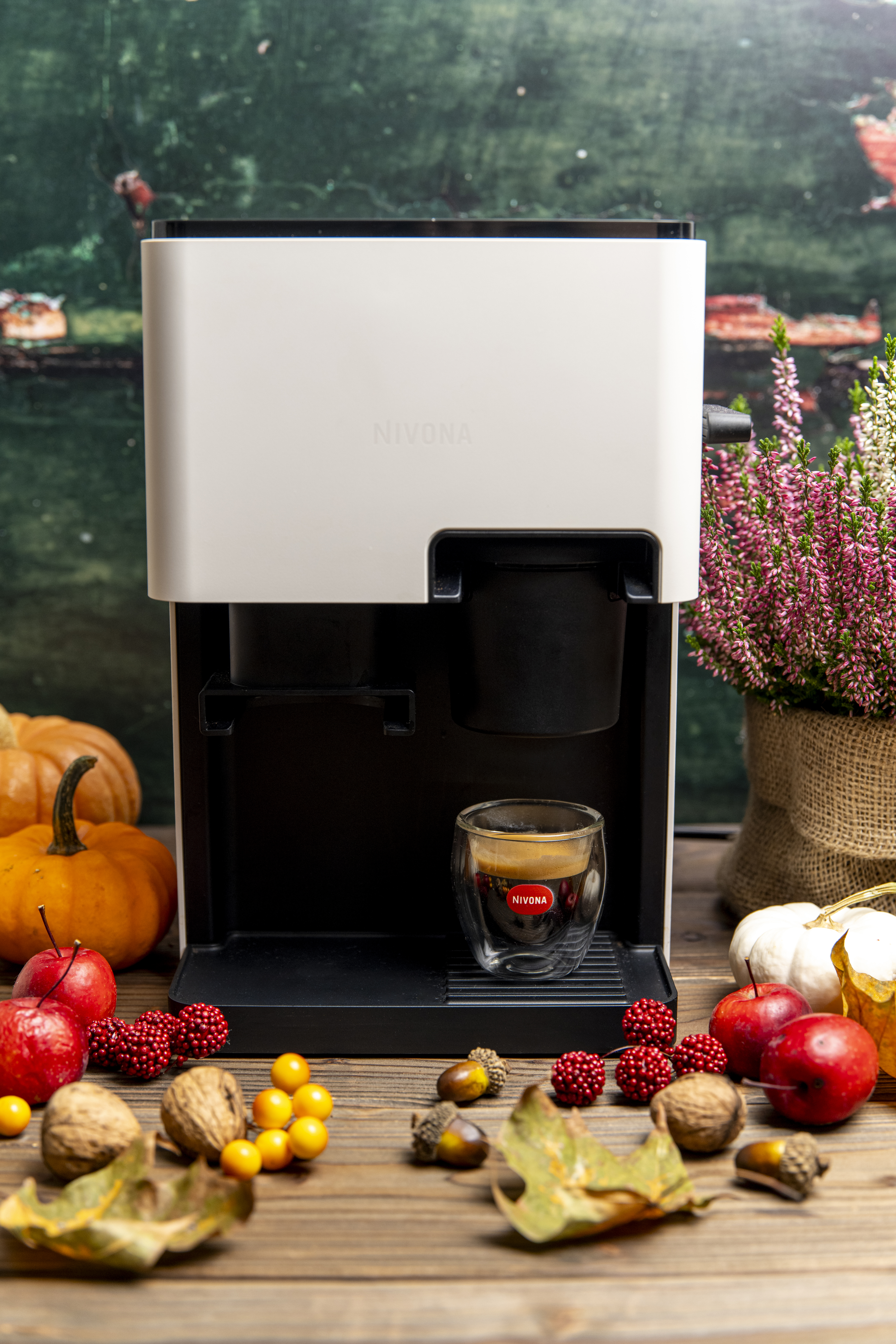 Ekspres do kawy Nivona z filiżanką espresso. Otoczony dyniami, jabłkami, orzechami i jesiennymi dekoracjami na drewnianym stole.