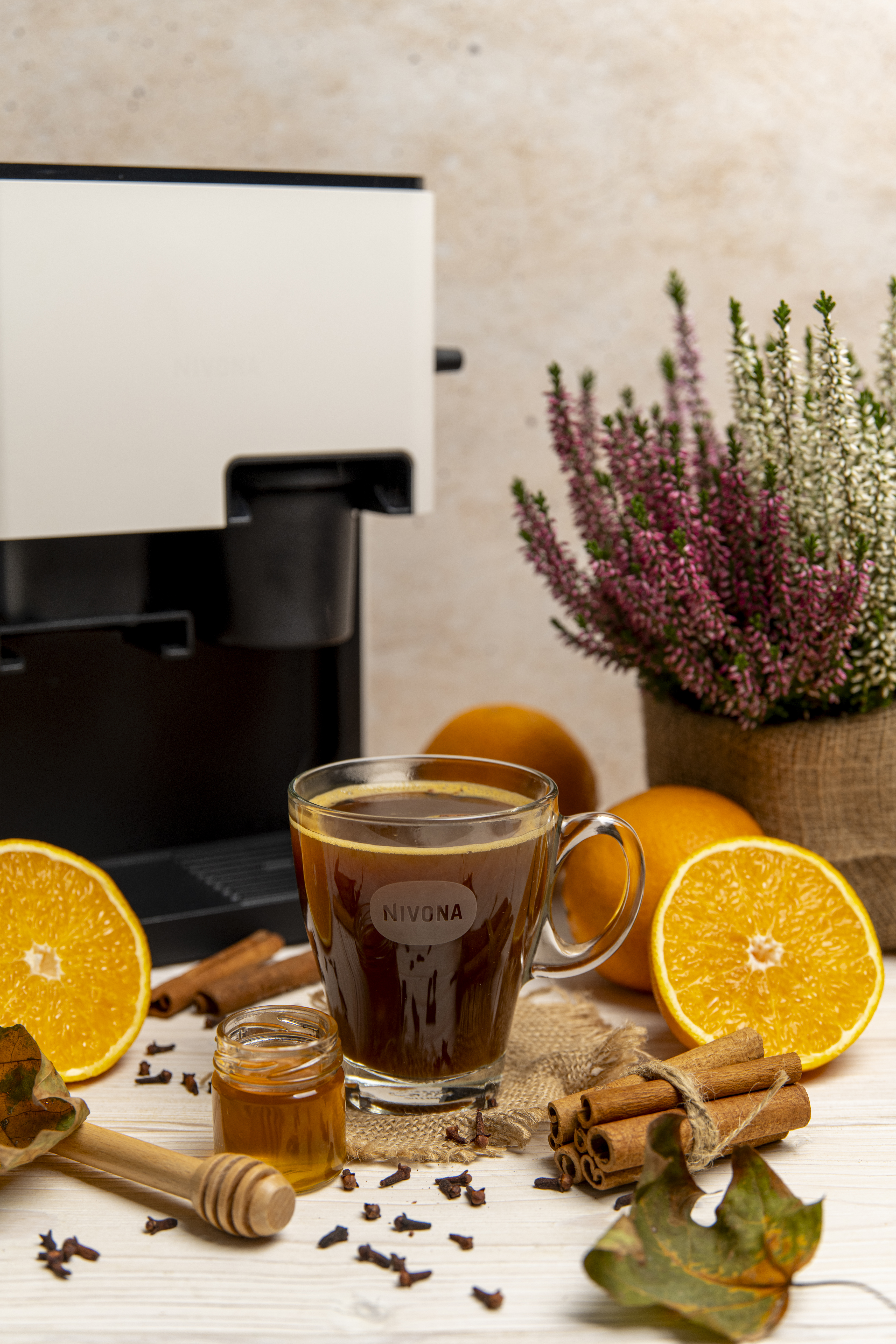 Filiżanka kawy z plasterkami pomarańczy, laskami cynamonu, miodem i doniczką. Ekspres do kawy w tle.