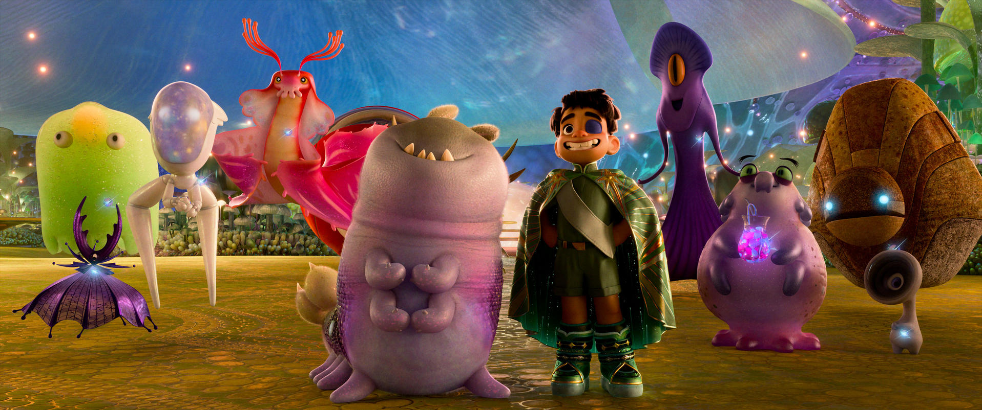 Ein Junge mit grünem Umhang steht mit verschiedenen Cartoon-Aliens. Lila, grüne und orangefarbene Kreaturen füllen die Szene, vor einem fantastischen Hintergrund.
