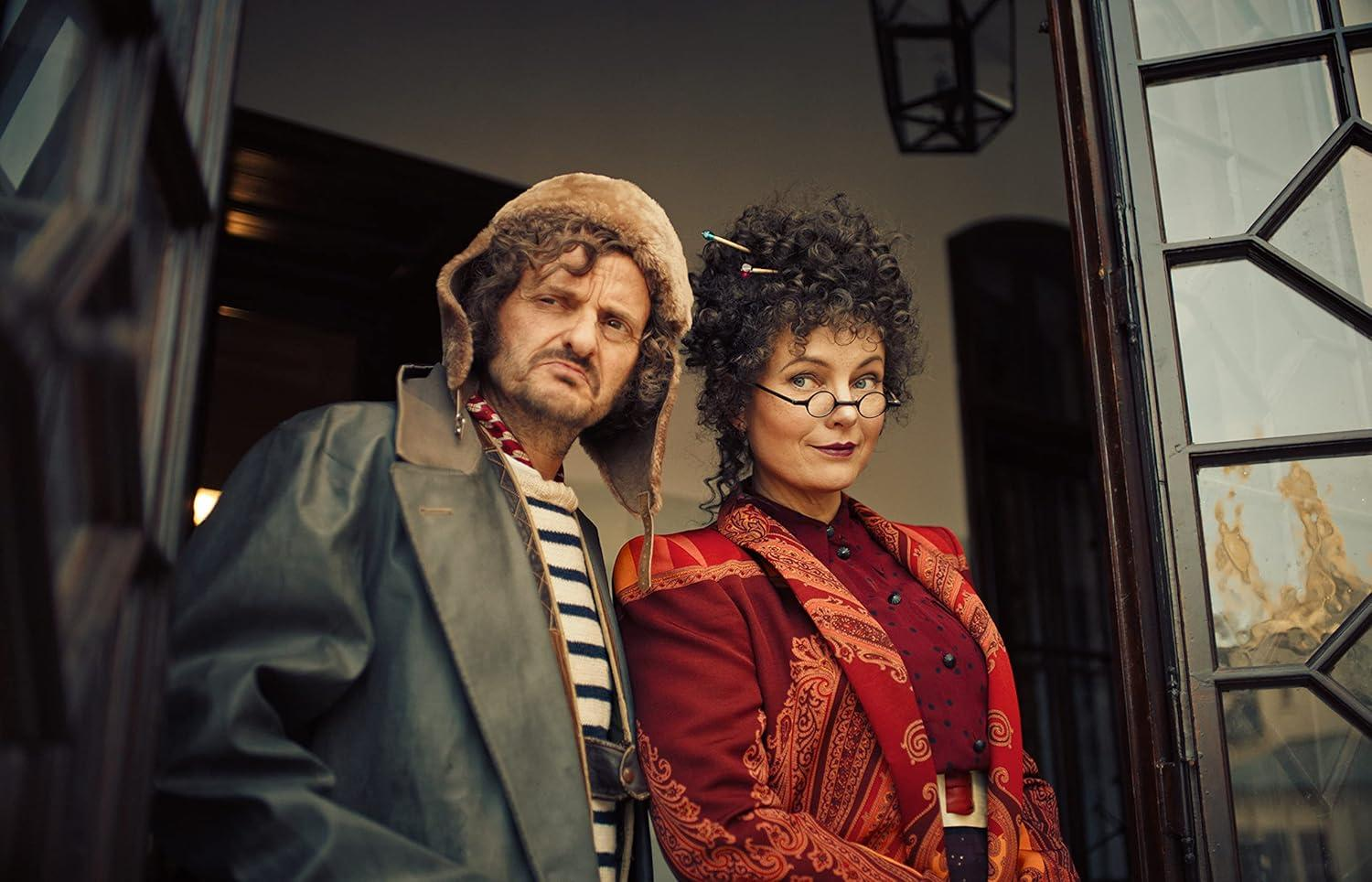 Ein Mann mit Hut und eine Frau mit Brille stehen nebeneinander.