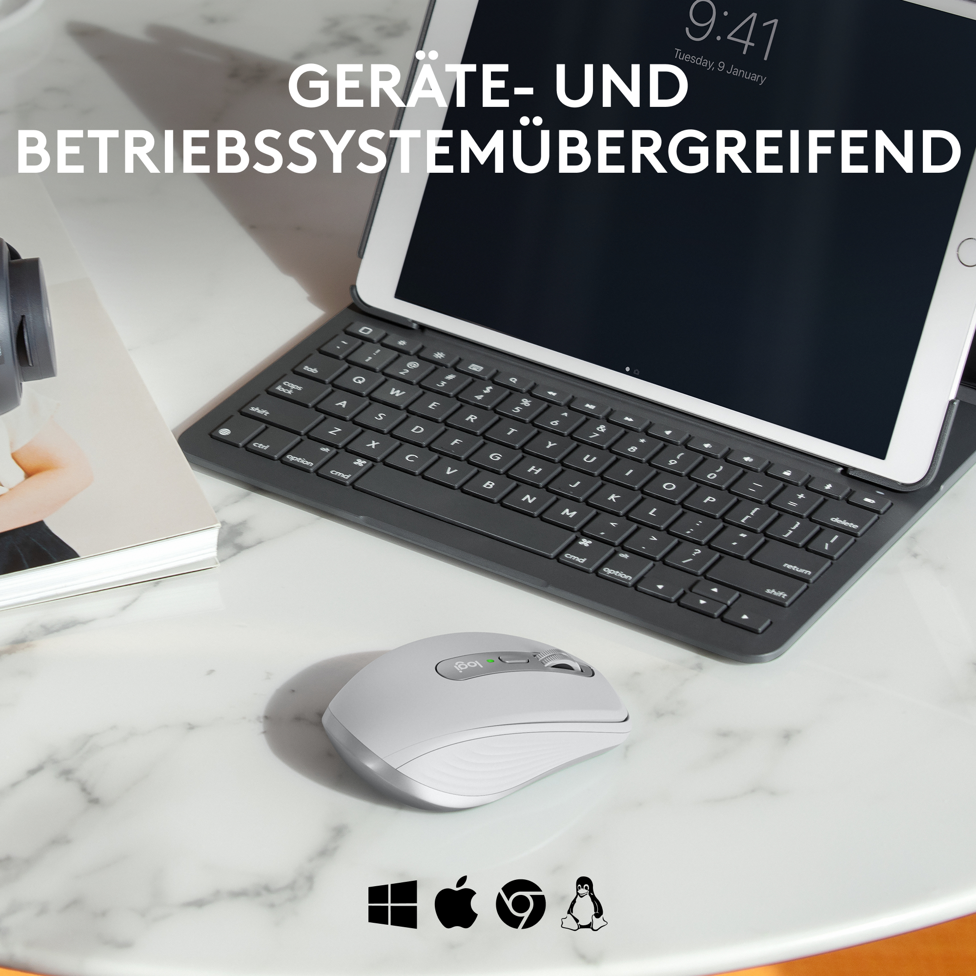 Ein Tablet mit Tastatur, eine Maus und Symbole von Betriebssystemen liegen auf einem weißen Marmortisch.