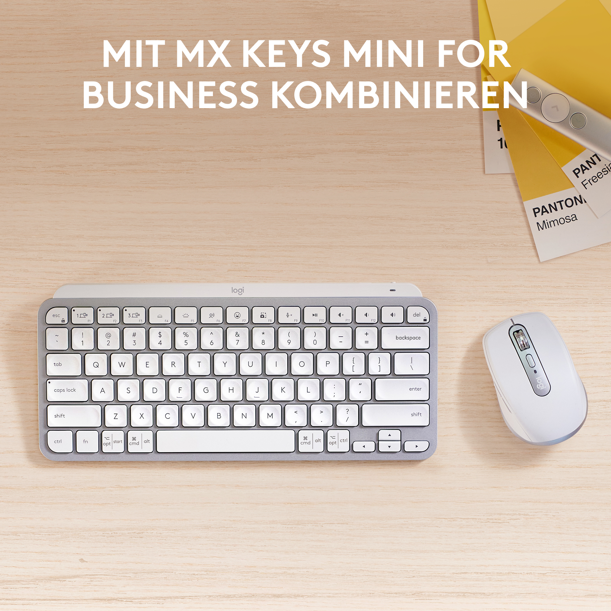 Eine Tastatur, eine Maus und Farbmuster liegen auf einer hellen Holzoberfläche. Die Tastatur ist silbern mit weißen Tasten. Die Maus ist weiß.