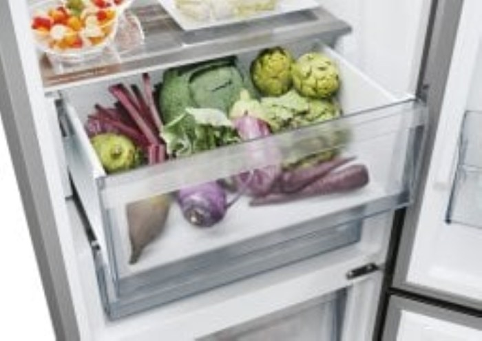 Wnętrze lodówki z otwartą szufladą na warzywa. Zawiera warzywa takie jak karczochy, sałata, buraki i inne świeże składniki.