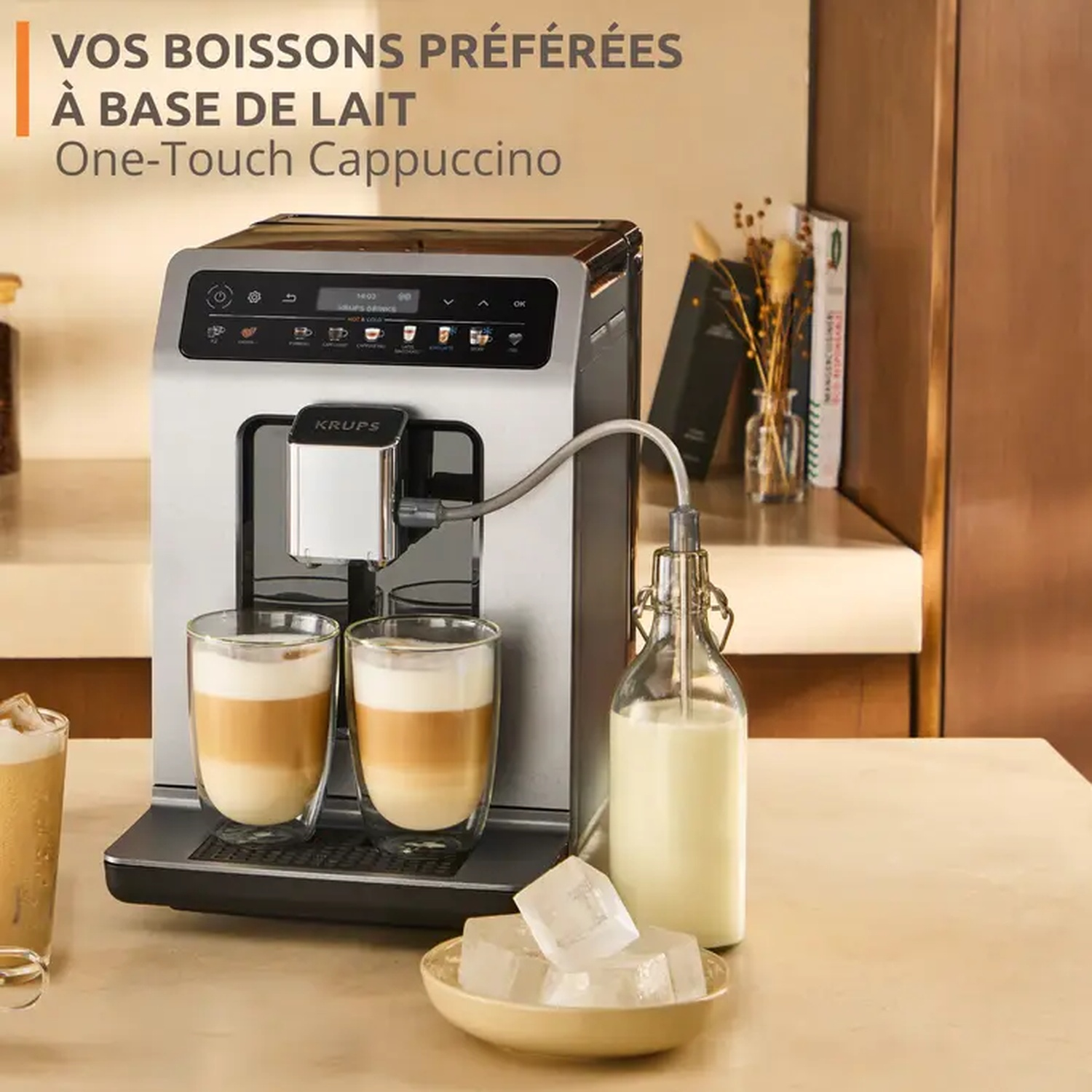 Une machine à cappuccino Krups avec deux verres de café en couches. Une bouteille de lait et des glaçons sont sur la table. Le texte dit 'One-Touch Cappuccino'.