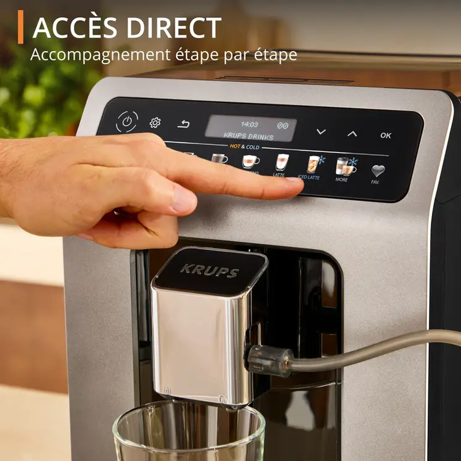 Une main appuie sur le bouton 'Iced Latte' d'une machine à café Krups. La machine est argentée et noire, avec un verre en dessous.