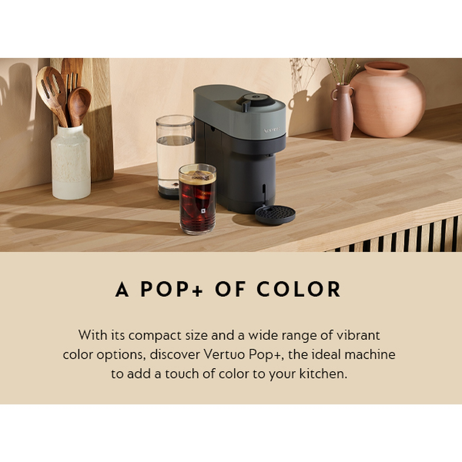 A coffee machine with a glass of iced coffee and water, wooden spoons, and two vases are on a wooden surface.