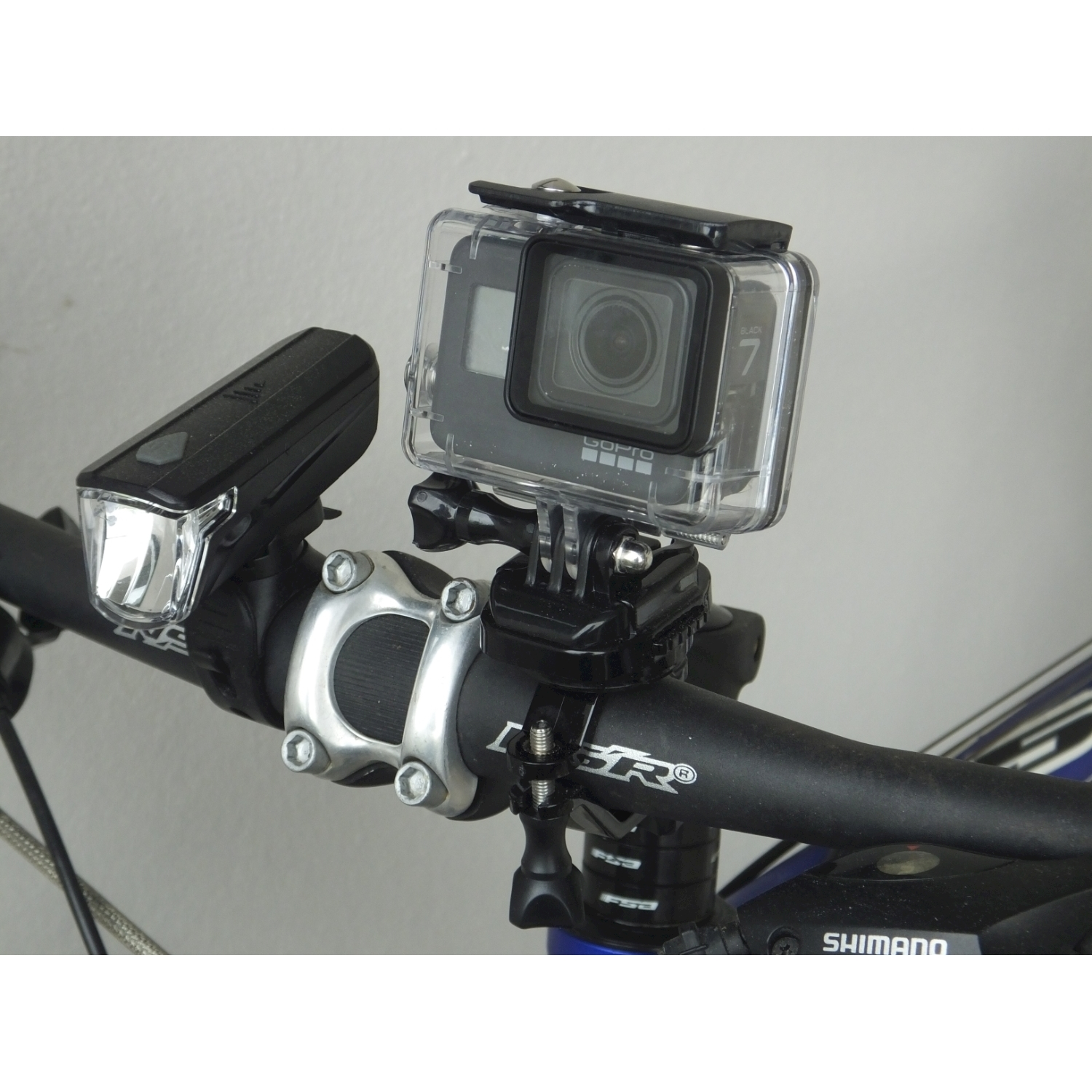 Una fotocamera GoPro in una custodia e una luce per bicicletta sono montate sul manubrio di una bicicletta. Il logo Shimano è visibile.