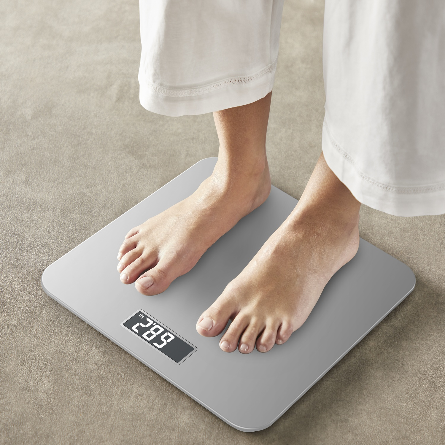 Person's feet on a digital scale, weight reading 289 kg. Wearing white pants. Beige carpet background.