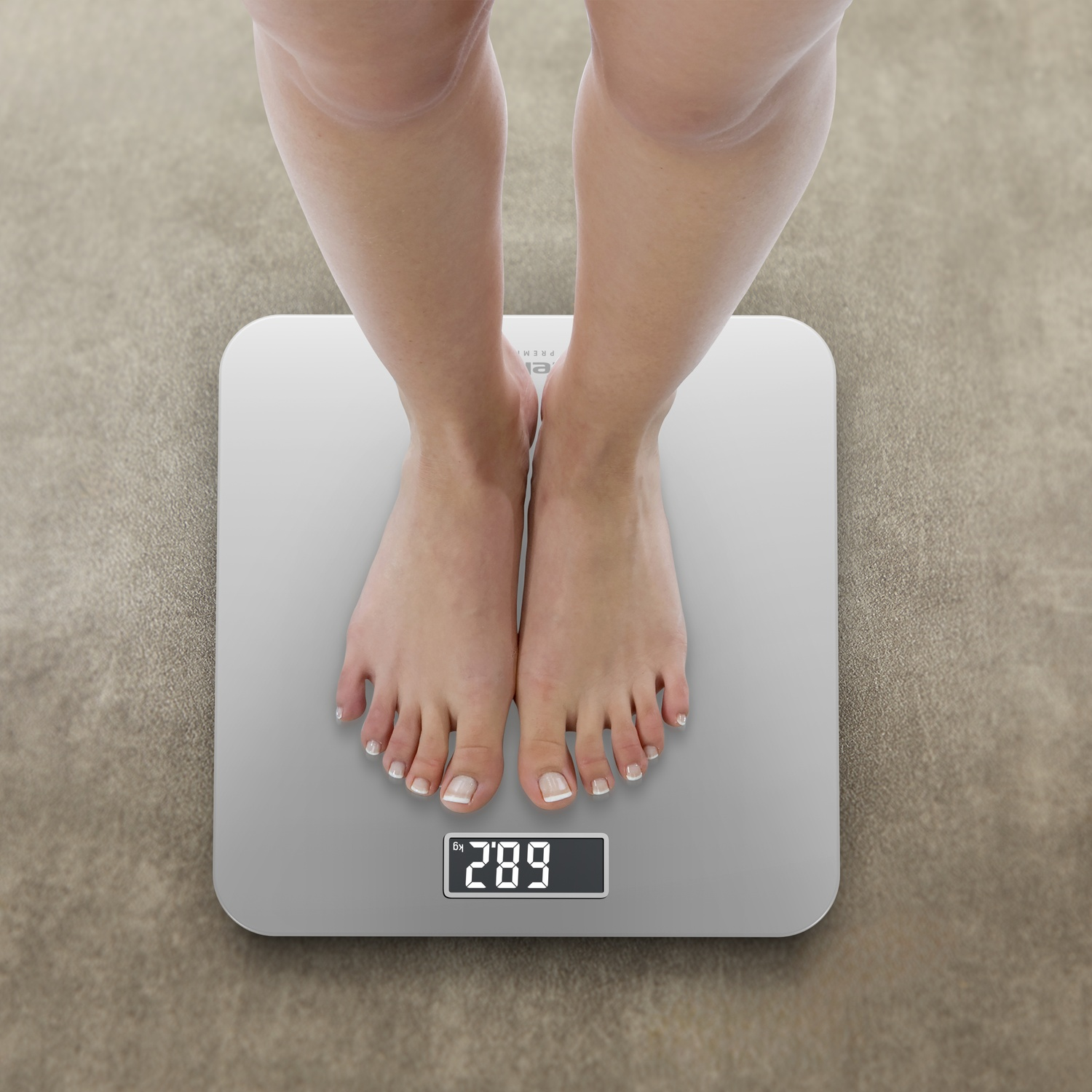 A person's feet stand on a digital scale. The scale reads 289. The background is a light brown carpet.