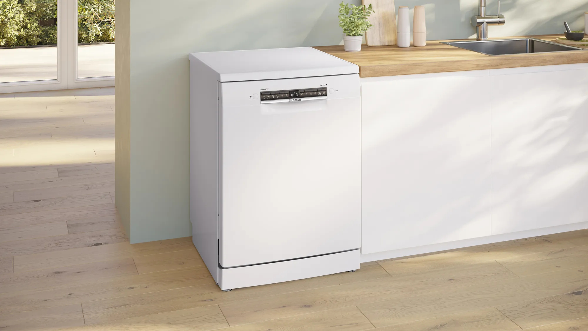 Lavavajillas Bosch blanco en una cocina. Suelo y encimera de madera. Plantas y fregadero visibles al fondo.