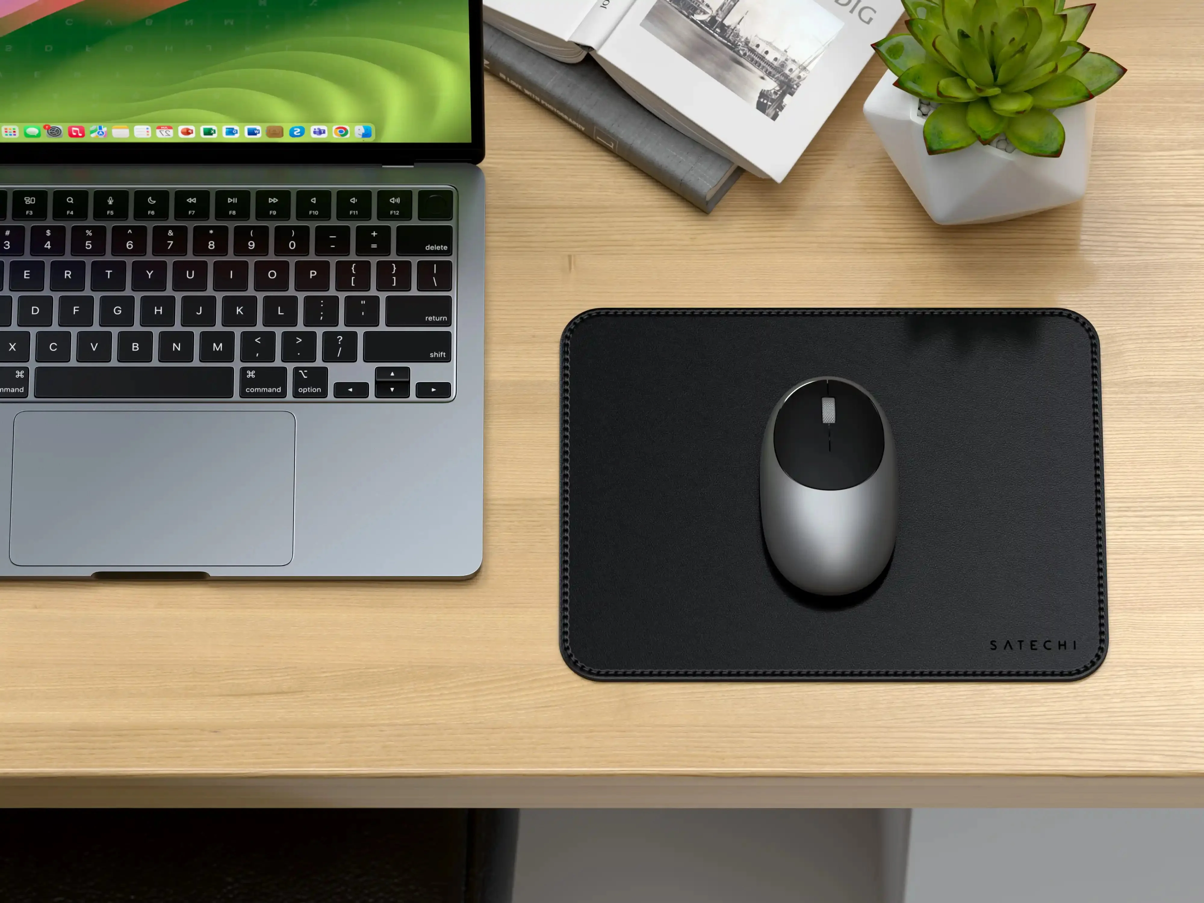 Un laptop, un mouse e un tappetino su una scrivania di legno. Sono presenti anche una piccola pianta e libri.
