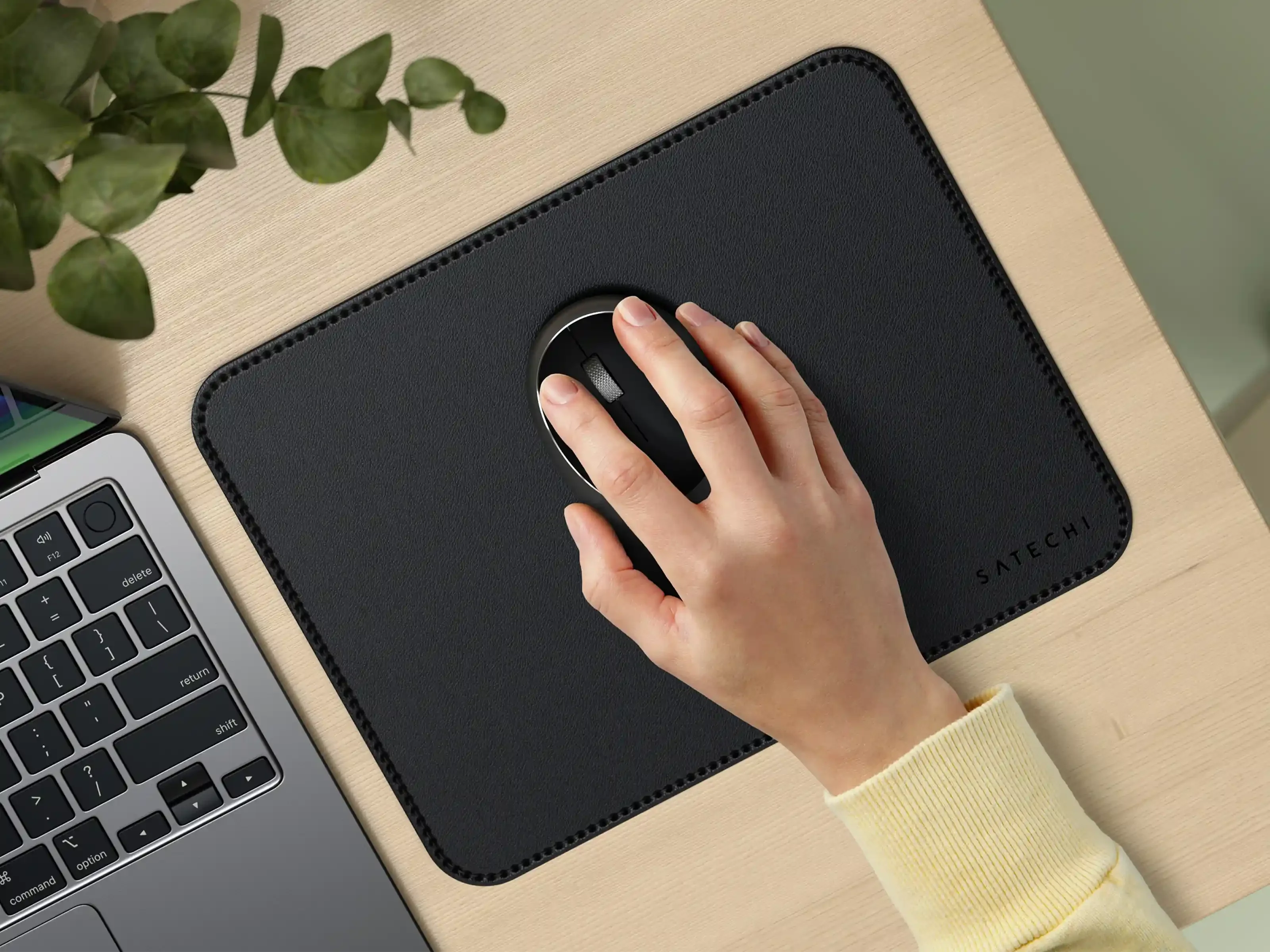 Una mano usa un mouse nero su un tappetino nero. Un laptop a sinistra.