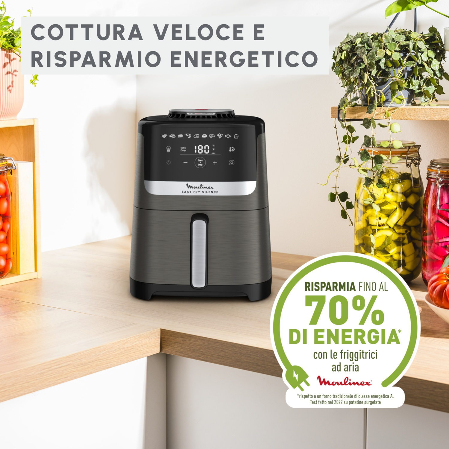 Una friggitrice ad aria su un bancone. Piante sullo sfondo, barattoli di cibo. Testo: Cottura veloce e risparmio energetico, risparmia fino al 70% di energia.