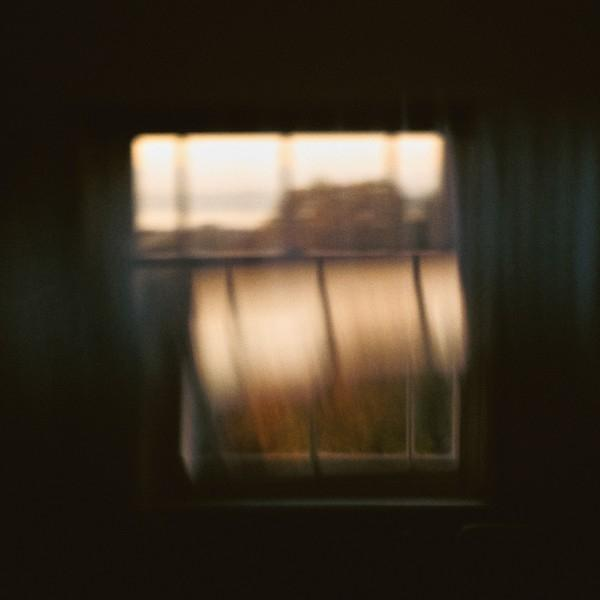 Ein Fensterblick. Verschwommenes Bild eines Fensters mit hereinströmendem Licht. Vorhänge rechts. Dunkles Interieur.