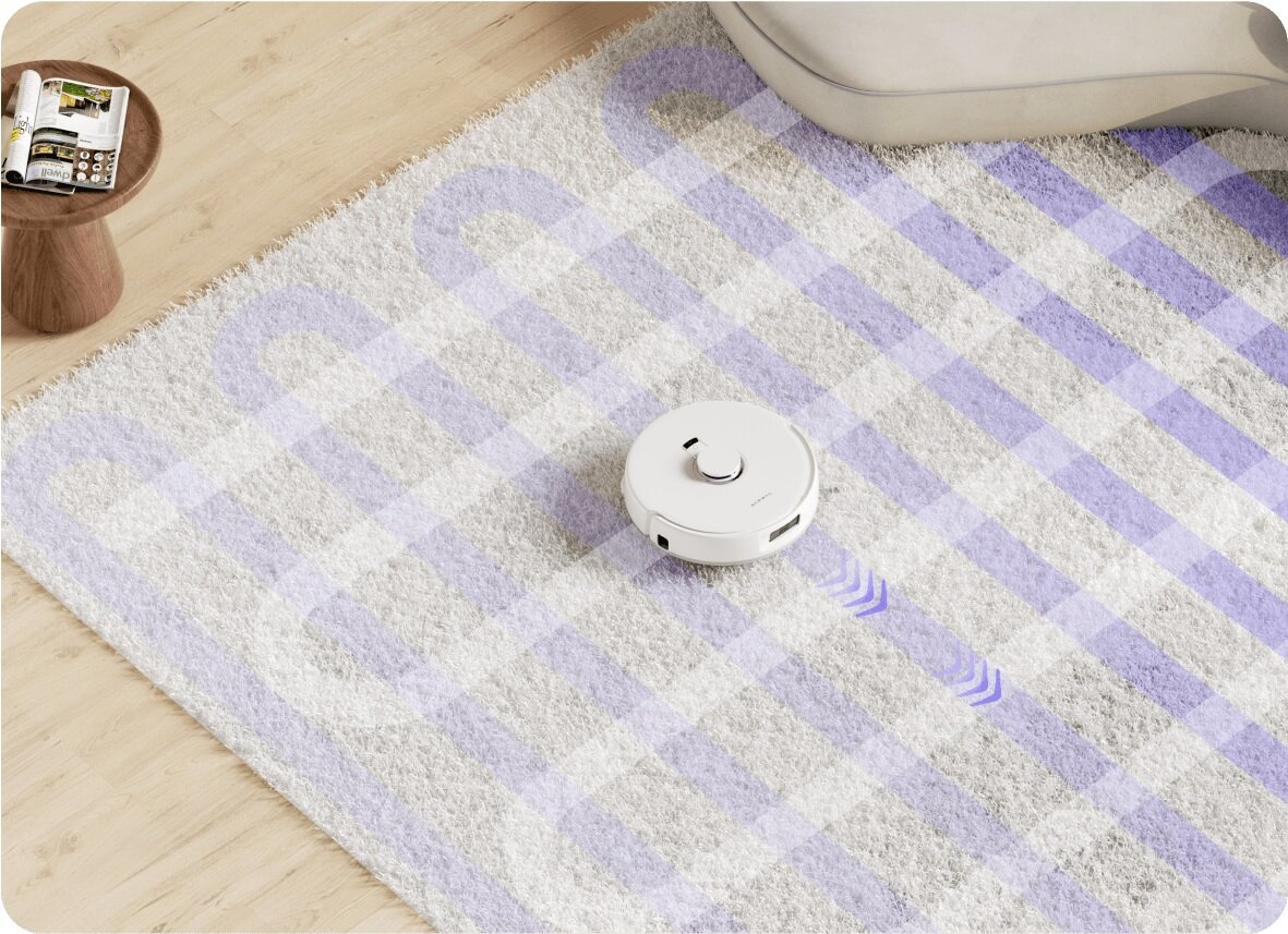 Biały robot odkurzający czyści dywan z fioletowym wzorem kraty. Widoczna jest również drewniana podłoga i mały stolik z czasopismem.