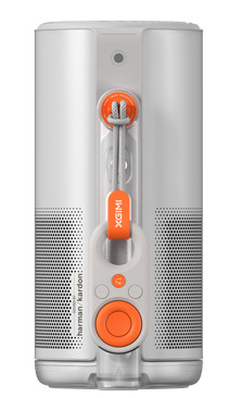 Biały głośnik cylindryczny z pomarańczowymi akcentami. Posiada pasek do przenoszenia i przyciski sterowania. Widoczna nazwa marki.