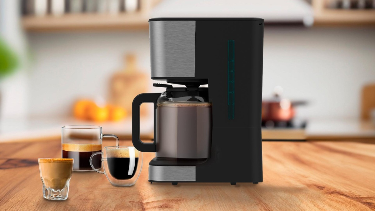 Ekspres do kawy ze szklanym dzbankiem, trzy szklanki z kawą. Drewniany stół w kuchni.