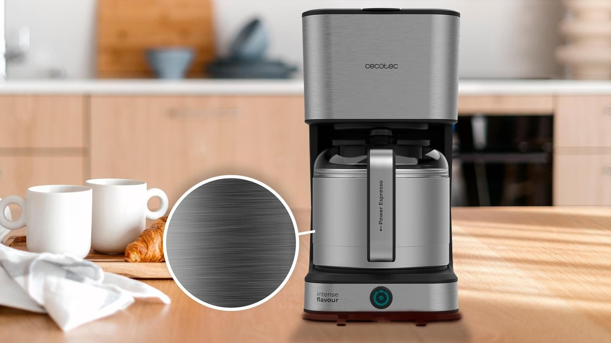 Srebrny ekspres do kawy ze szklanym dzbankiem. Dwie białe filiżanki i rogalik na drewnianej desce. Tło jest rozmyte.