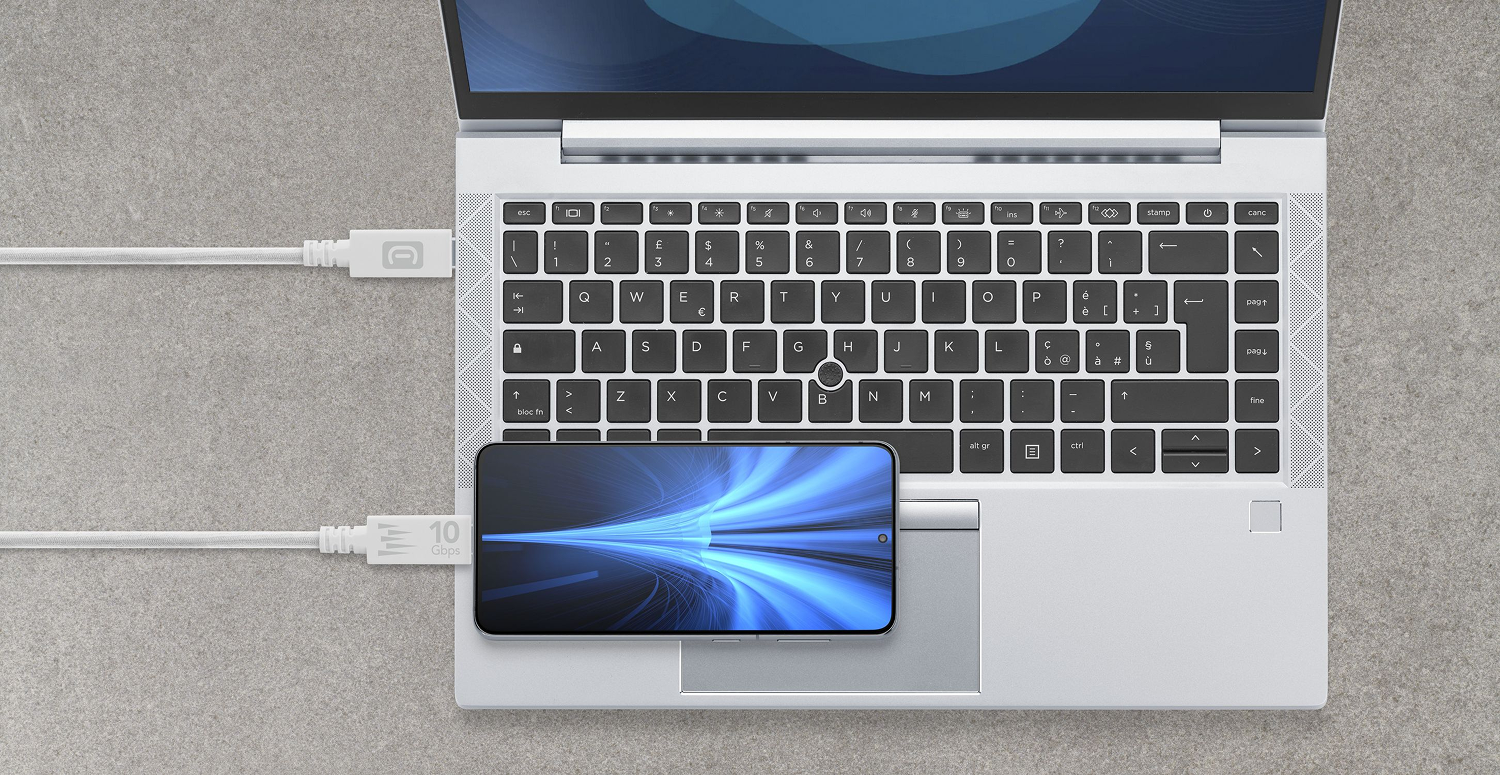 Un portátil con un smartphone en el panel táctil. Ambos están conectados con cables blancos. El teléfono muestra un gráfico de luz azul.