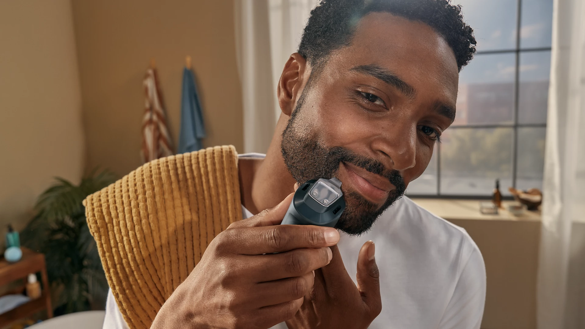 Un uomo si rade la barba con un rasoio elettrico. Tiene un asciugamano. Lo sfondo mostra un bagno.
